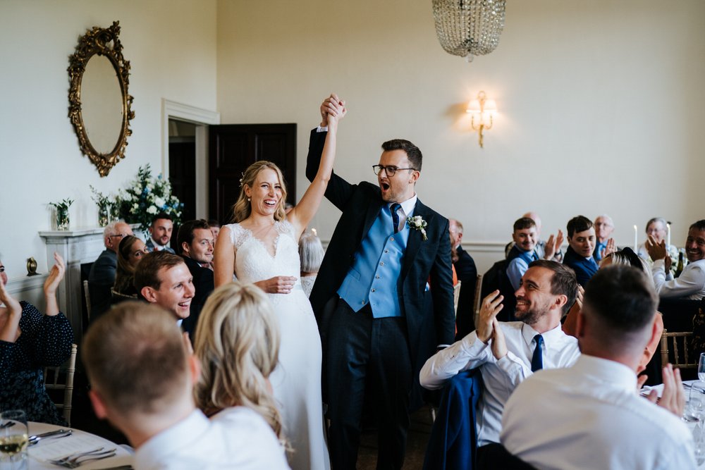 Bride and groom enter reception room and throw their hands in the air during Pynes House wedding in Exeter