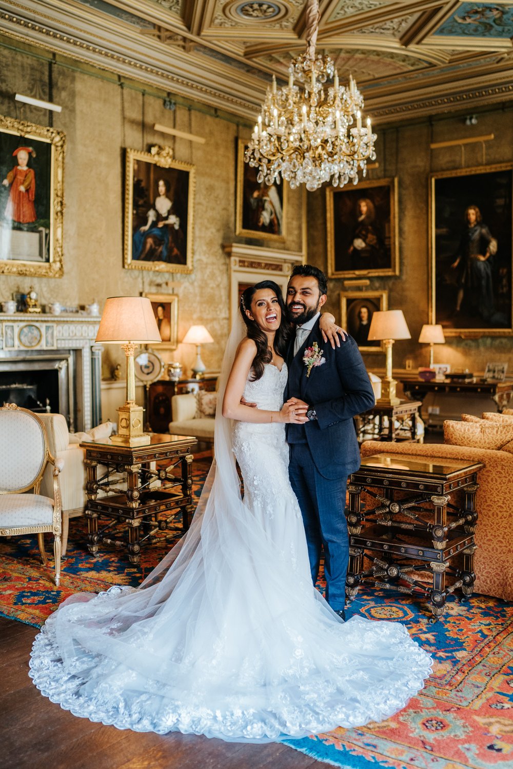 Bride, with carefully styled wedding dress, poses with groom in gorgeous, ornate room in Syon Park