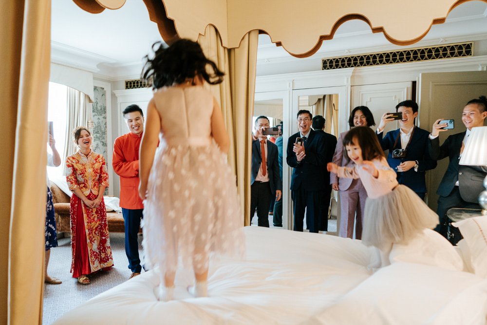 Two kids jump on the wedding while bride and groom, dressed in traditional Chinese attire, look on and smile
