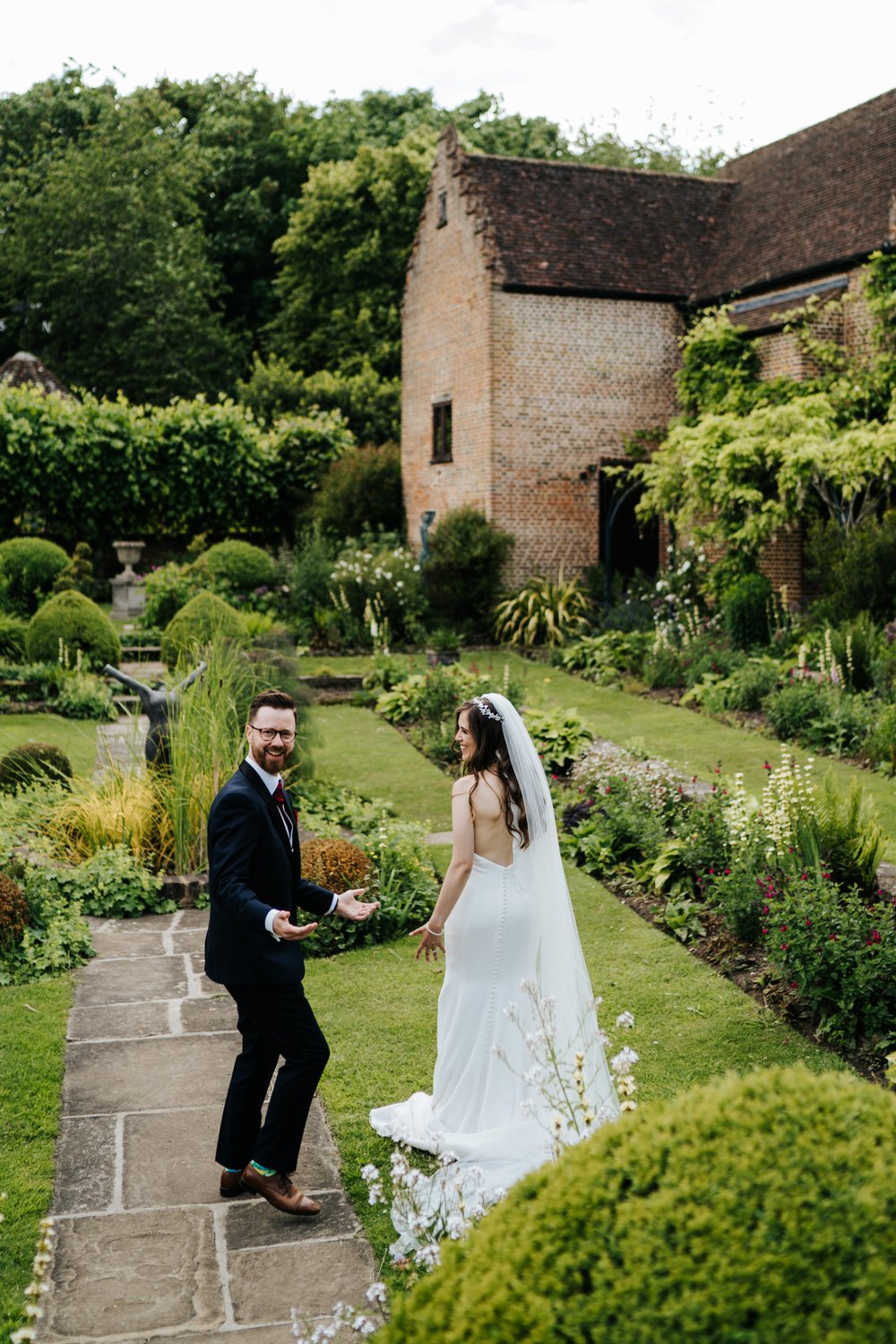 Bride and groom walk away from camera as groom holds hands up in confusion after throwing bride's veil during Chenies Manorhouse wedding