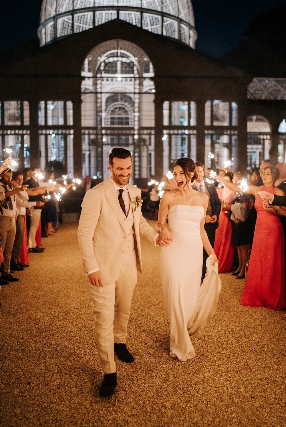 Bride and groom hold hands as they exit Syon Park's Great Conservatory through a sparklers tunnel