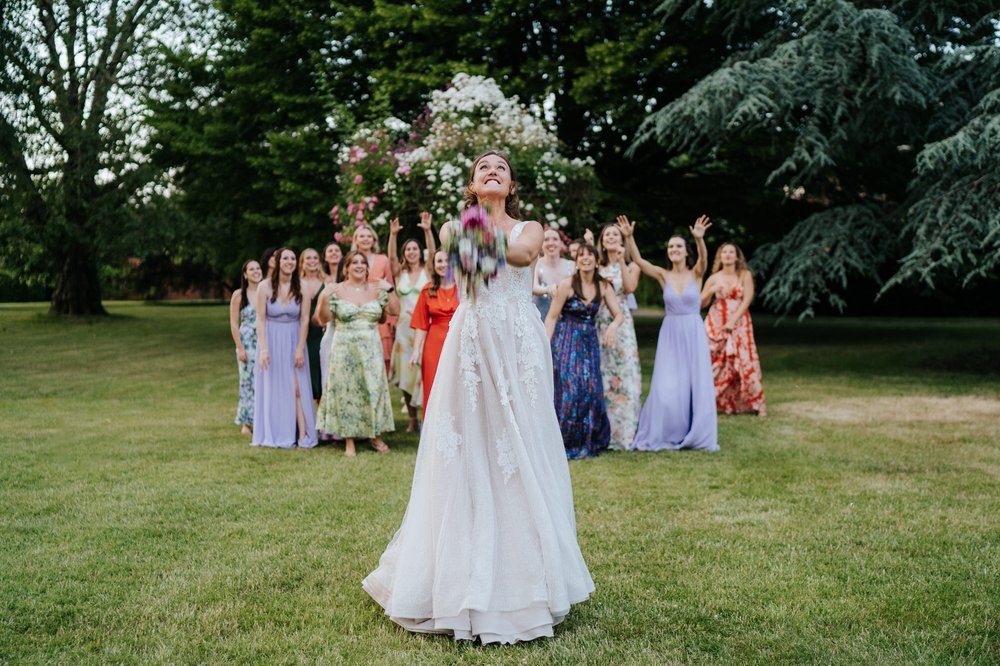 Bride throws bouquet at group of girlfriends standing behind her during Hampton Court Palace Garden Room wedding