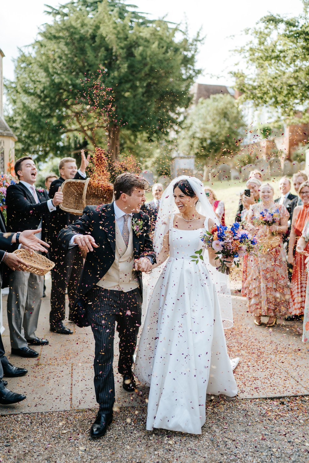 Bride and groom, dressed impeccably, exit church in Woodbridge through tunnel of confetti