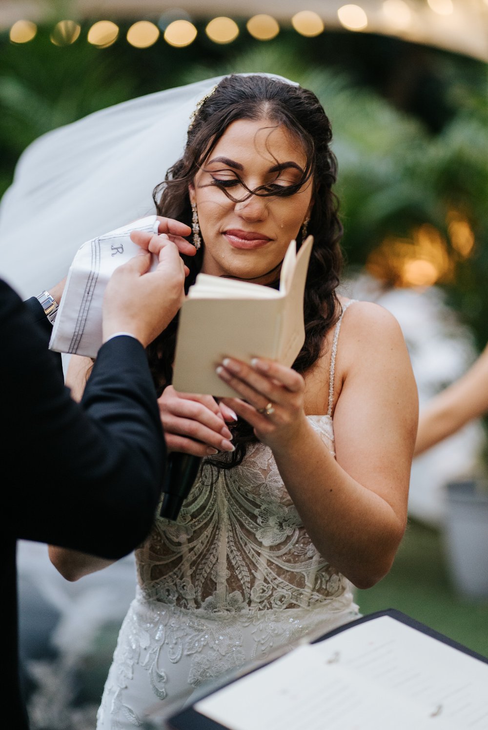 Bride has wind blow hair in her face as groom reaches in with his handkerchief to wipe the tears that are streaming down her face during wedding ceremony at Villa Woodbine in Miami