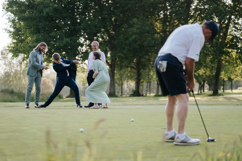 Group of guests have fun and pretend to play golf as actual golfer, in foreground, puts a hole in one