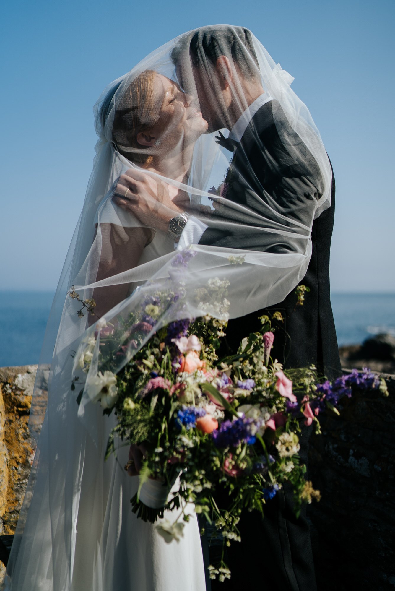 Ethereal portrait of bride and groom embracing each other under the veil as the sunlight hits her face