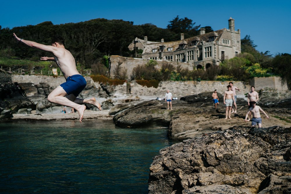 Wide photograph of groom jumping off cliffs and into the sea at Prussia Cove in Cornwall hours before he is set to get married