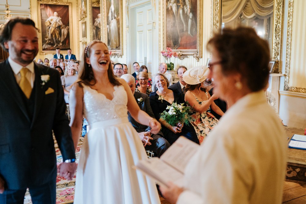 Bride, groom and congregation cannot contain their laughter as registrar says something funny at Goodwood House wedding ceremony