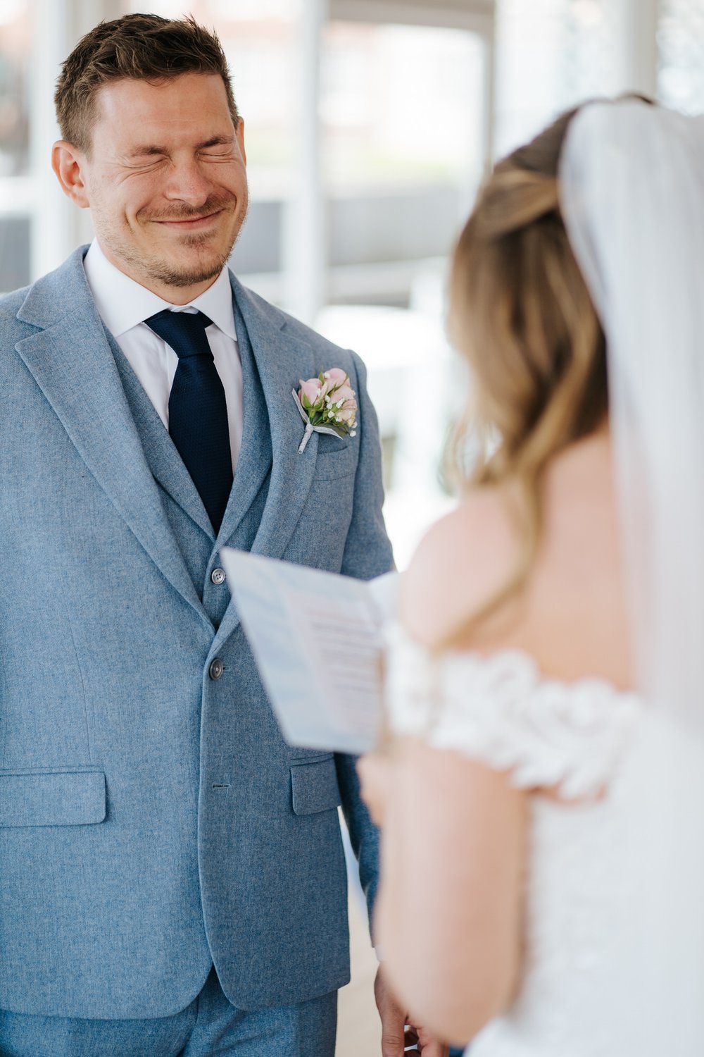Close-up shot of the groom, squeezing his eyes in embarrassment as the bride reads her personal wedding vows during ceremony