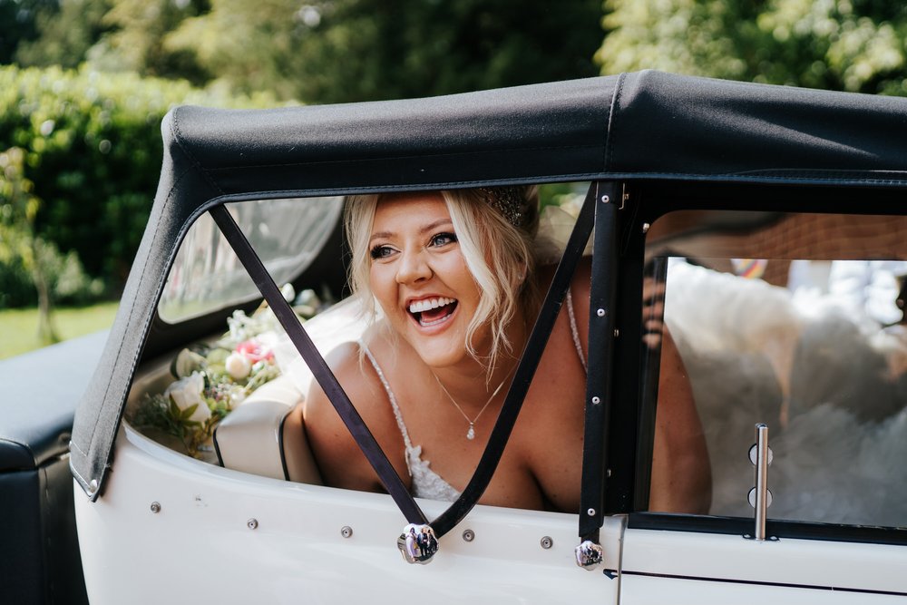 Bride, joyful and charismatic, peeks out of wedding car and smiles before heading off to the wedding ceremony