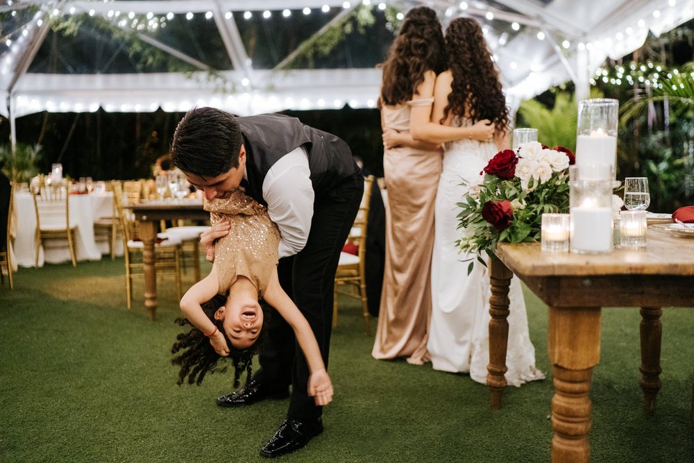 Groom plays around with his niece while bride takes a photo with a friend in the background