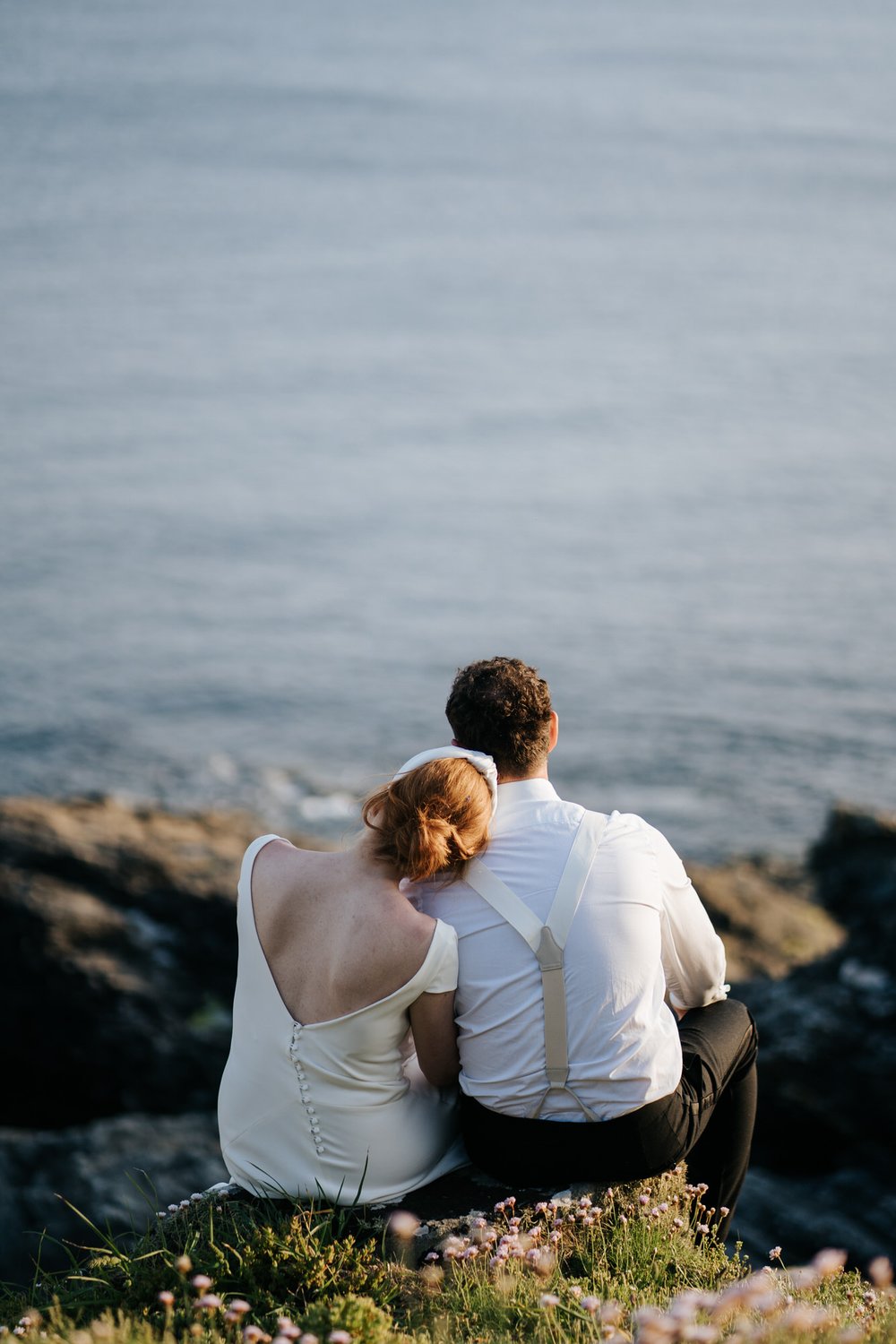 Bride leans her head on groom's shoulder as they both share an intimate moment sitting and looking out at the Cornish coast from Prussia Cove