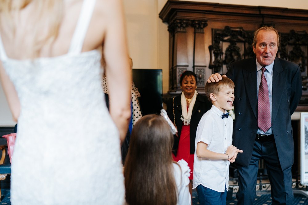 Father of the bride jokes around with her son as he pats his head and bites his tongue 