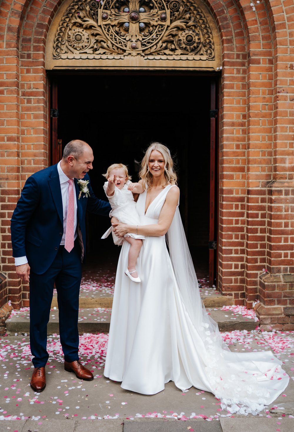 Bride and groom hold their daughter for wedding photo while the daughter squeals in excitement