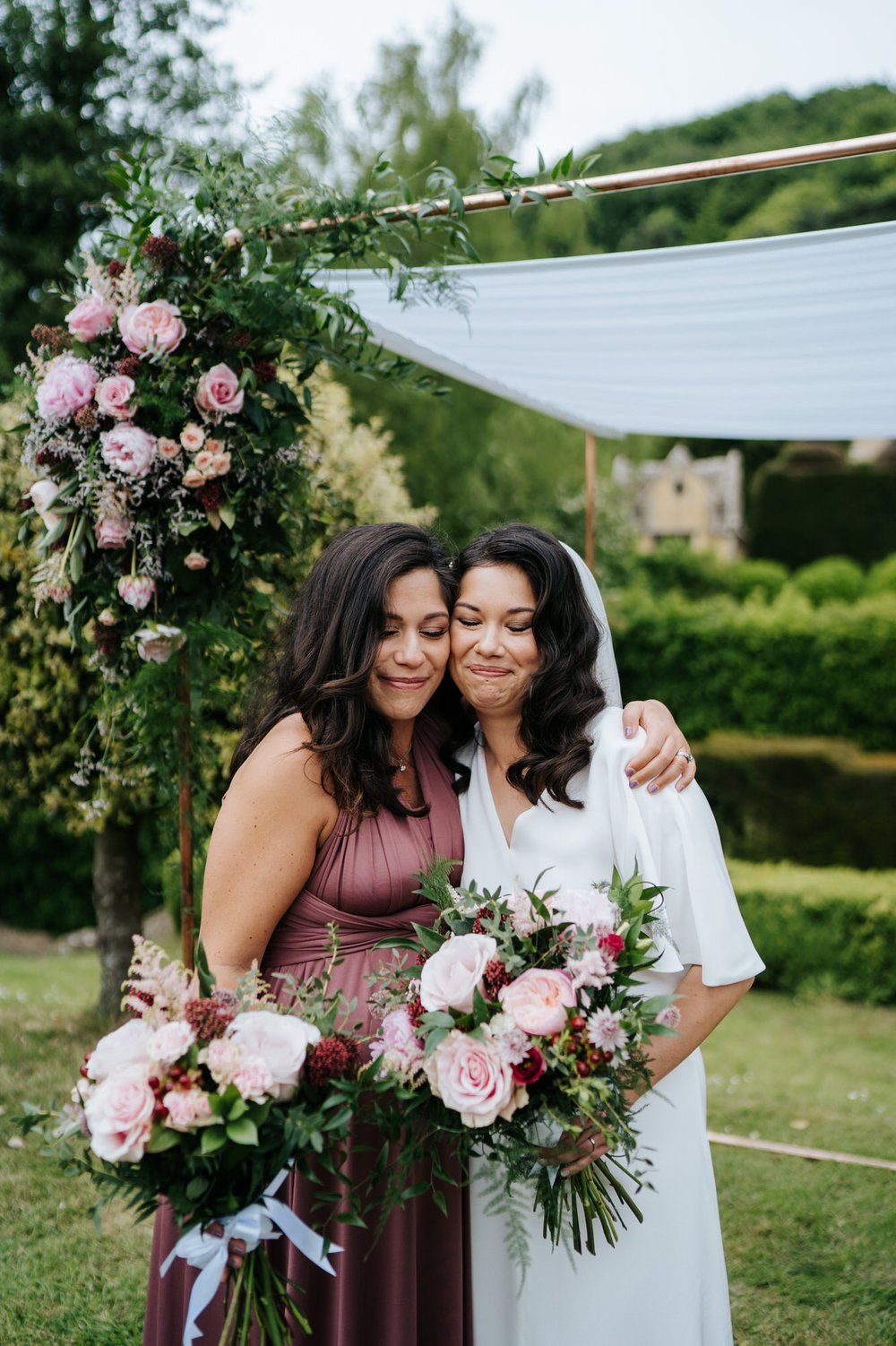 Bride and bride's sister embrace each other lovingly during candid moment in between staged family photos 
