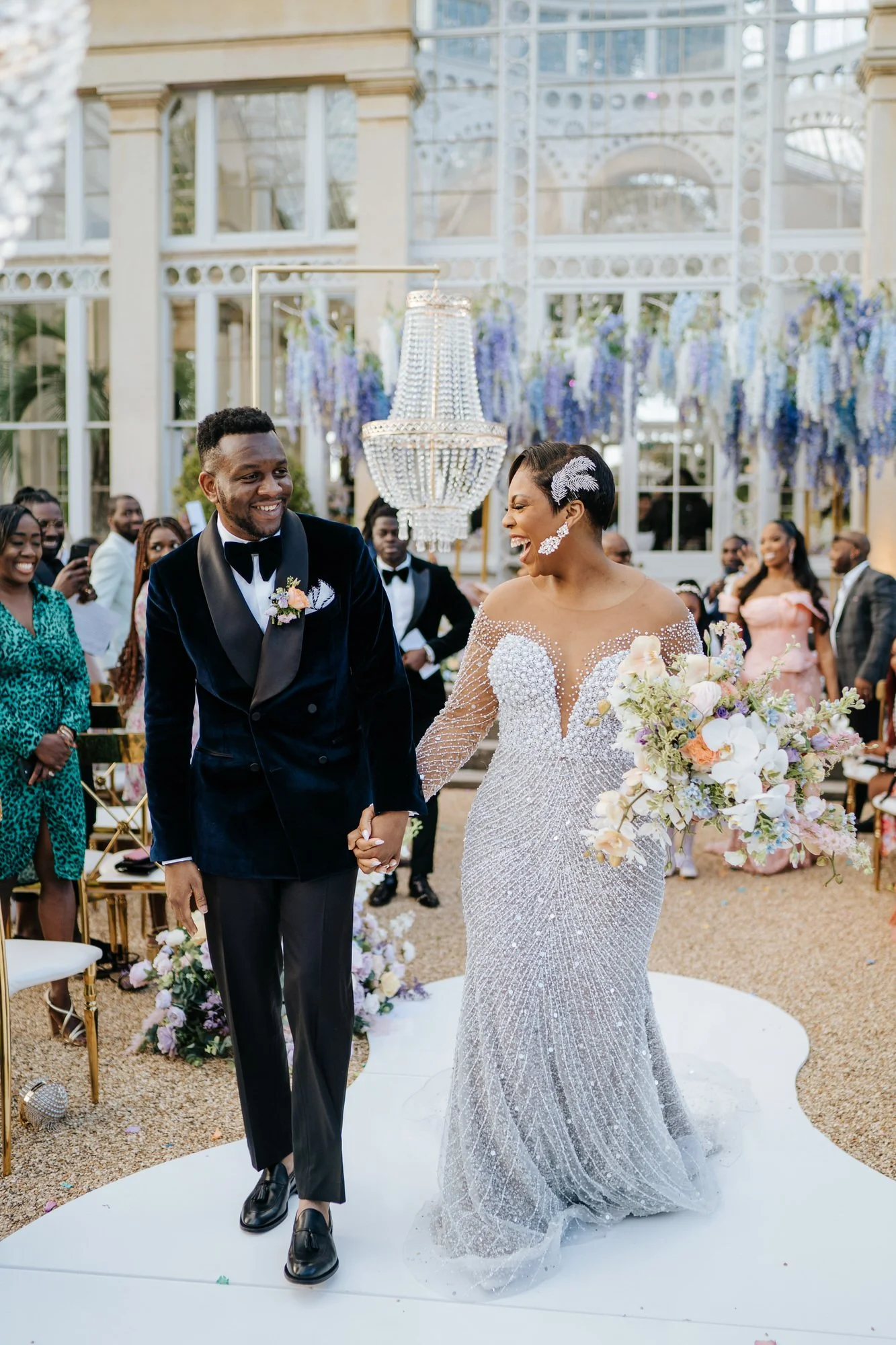 Bride and groom, hand in hand, look at each other and smile as they exit wedding ceremony at Syon Park