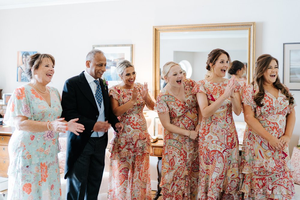 Bride's parents and her bridesmaids react with joy and surprise as they see the bride in her wedding dress for the first time