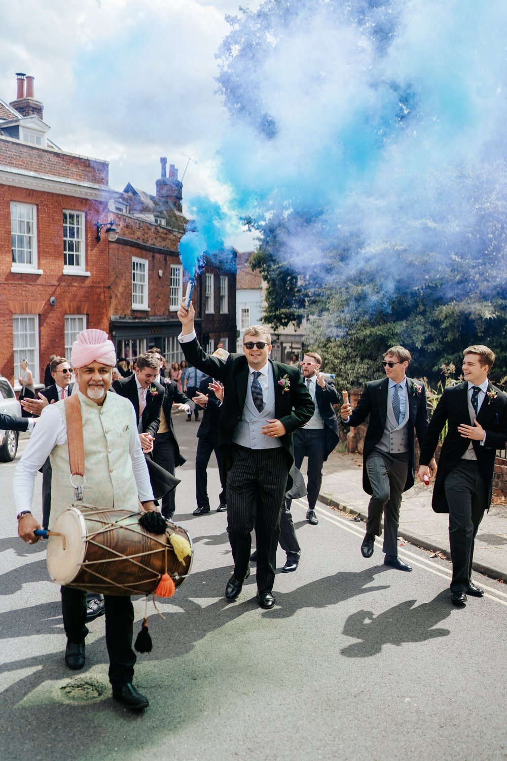 Baraat for the groom begins as groom's brother holds a blue smokebomb above his head while walking towards the crowd waiting at the top of the hill