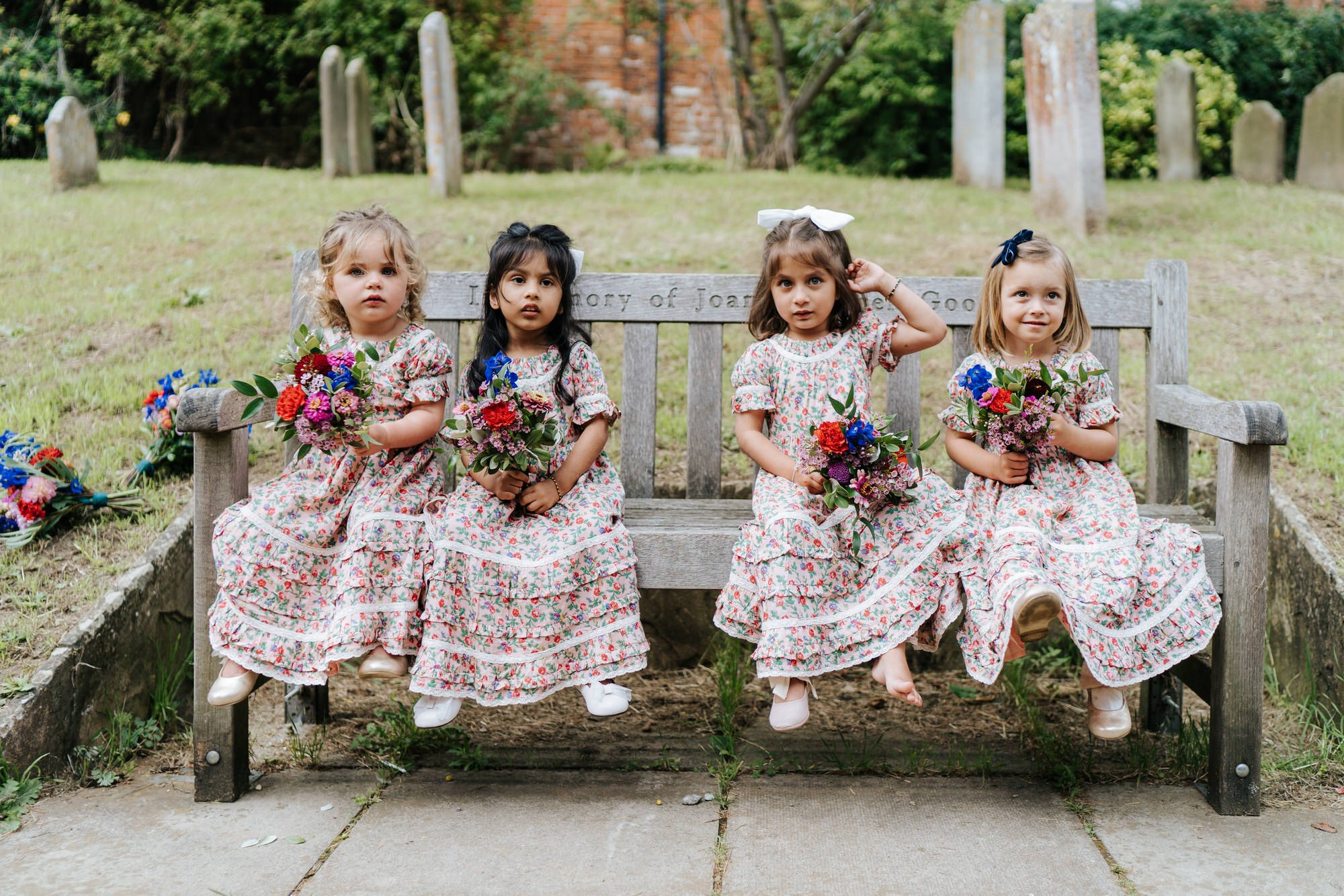 Four little bridesmaids in colourful dresses hold their flowers and pose for the camera