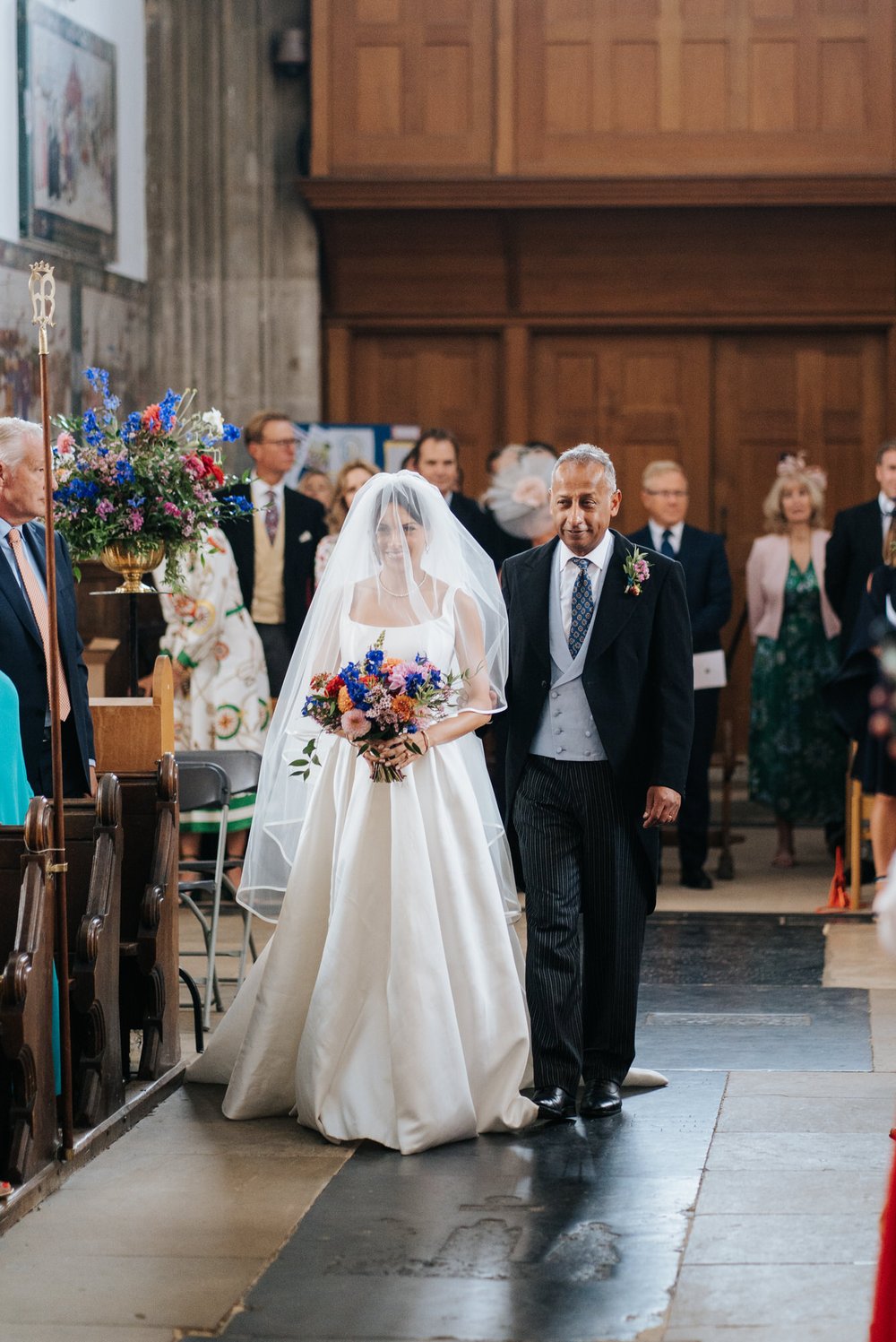 Bride, covered in veil, walks down the aisle with her father
