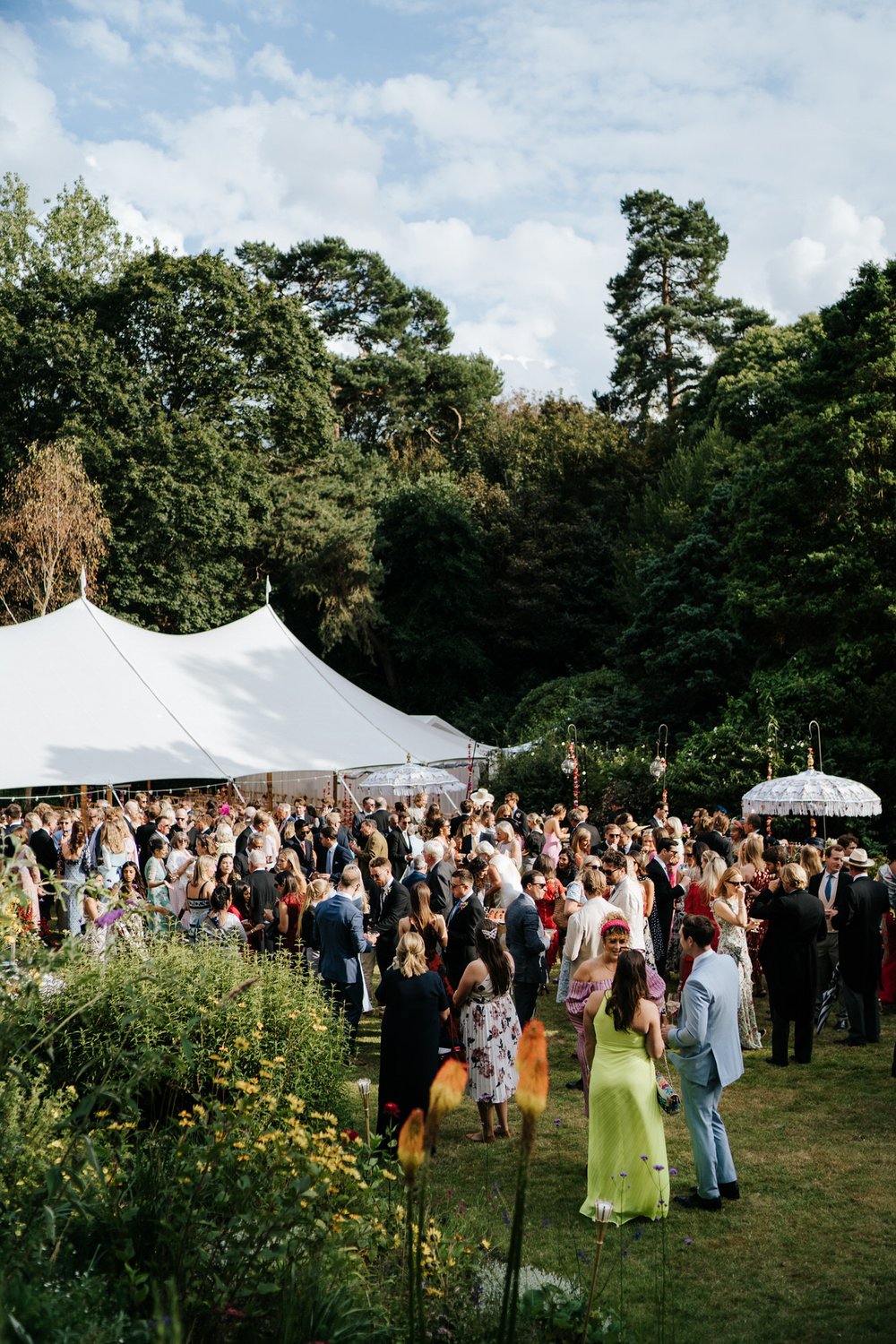 Wide photograph of marquee in the background with guests enjoying the drinks and canapes in the garden at British garden wedding