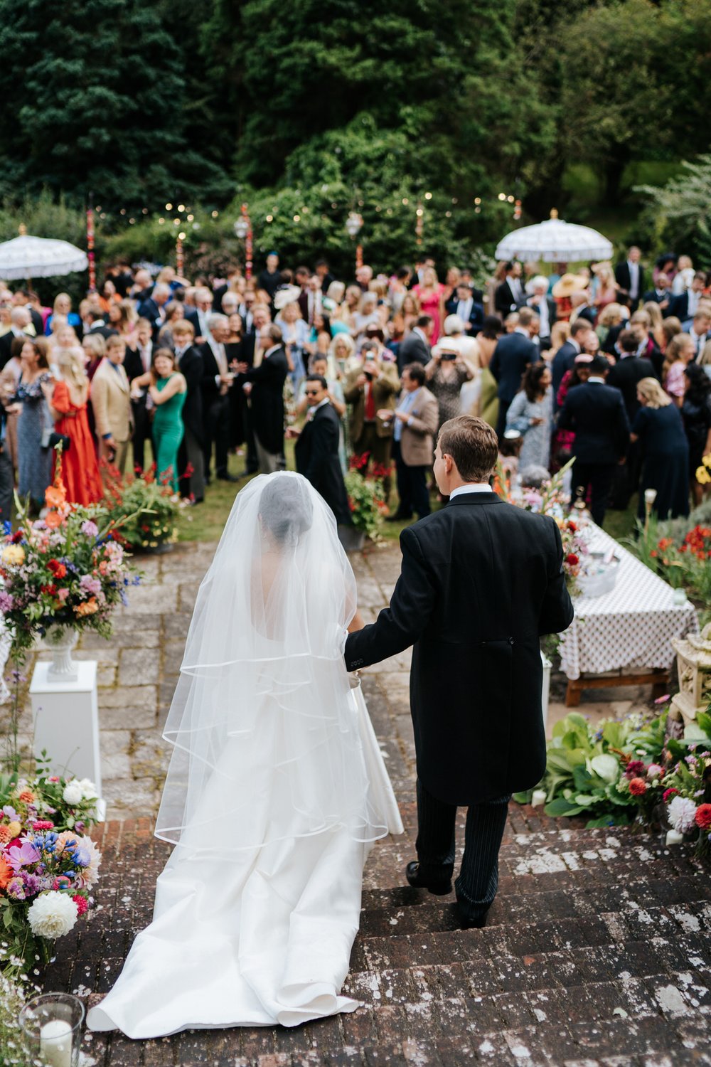 Bride and groom walk down steps and into their wedding reception as guests clap