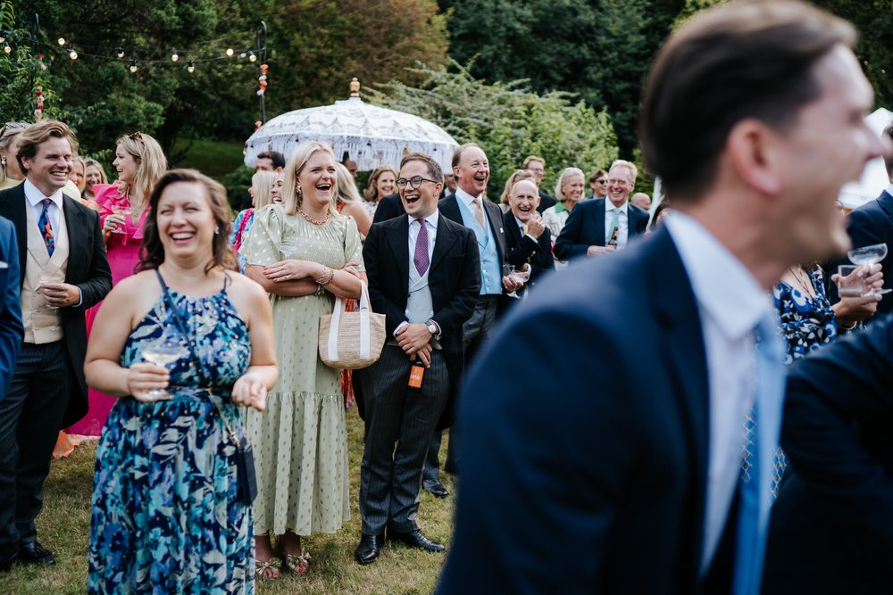 Group shot of guests cackling and laughing during wedding speeches taking place in garden