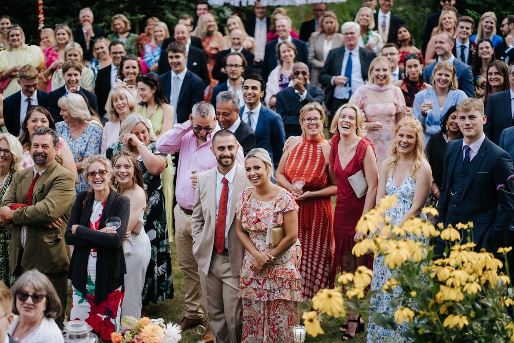 Wide photograph of wedding guests attentively listening to wedding speeches taking place during drinks and canapes in British garden wedding