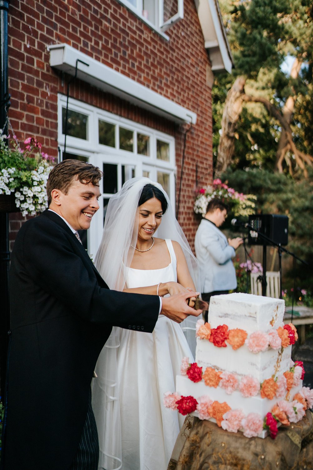 Bride and groom cut the white wedding cake which is decorated with red and pink flowers