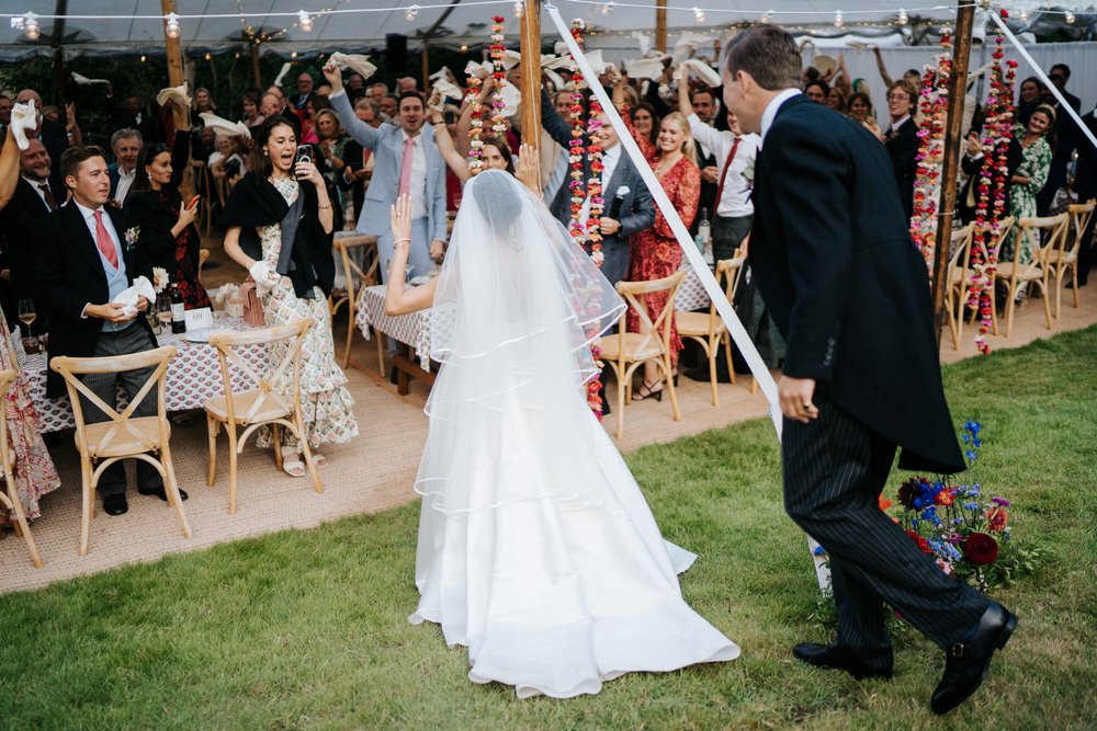 Bride and groom enter marquee as guests wave all their napkins in the air