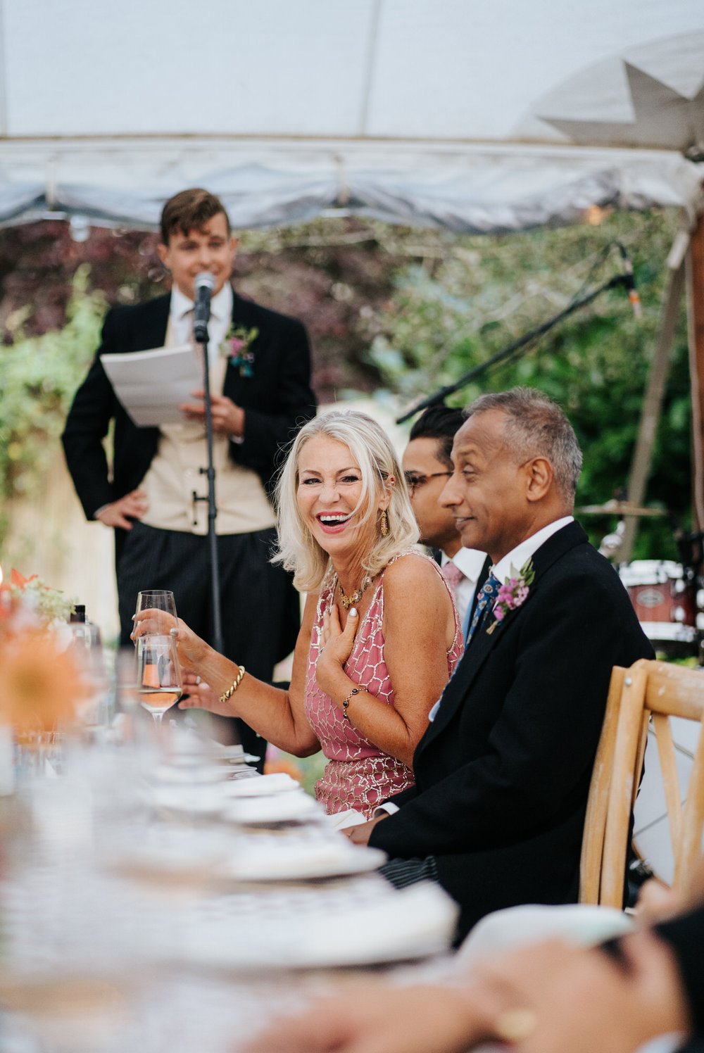 Groom's mother laughs as her son delivers his wedding speech inside marquee