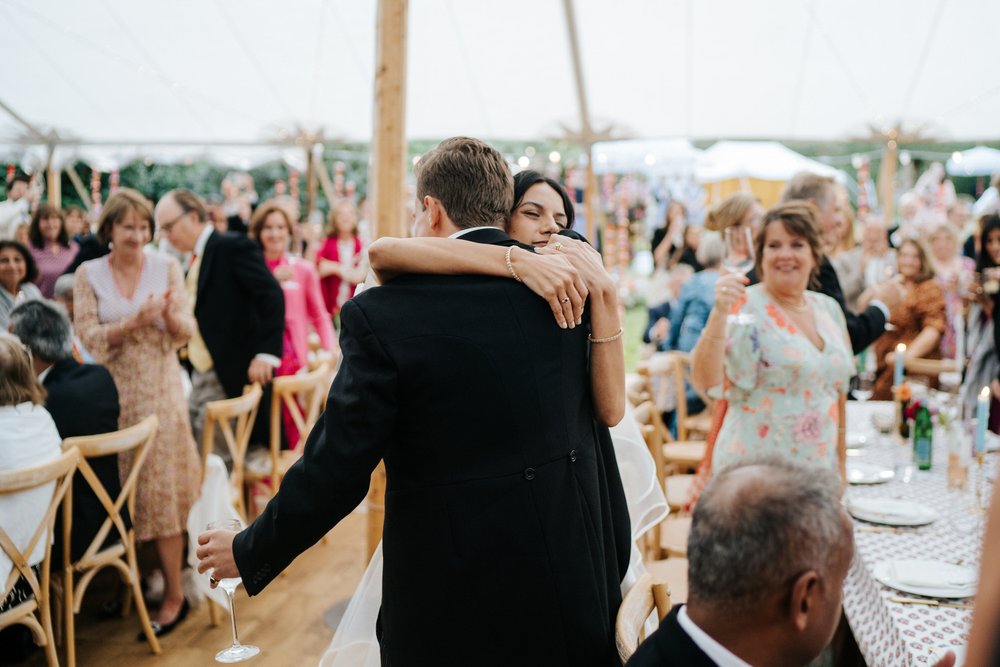 Bride hugs the groom after he finishes his wedding speech inside marquee
