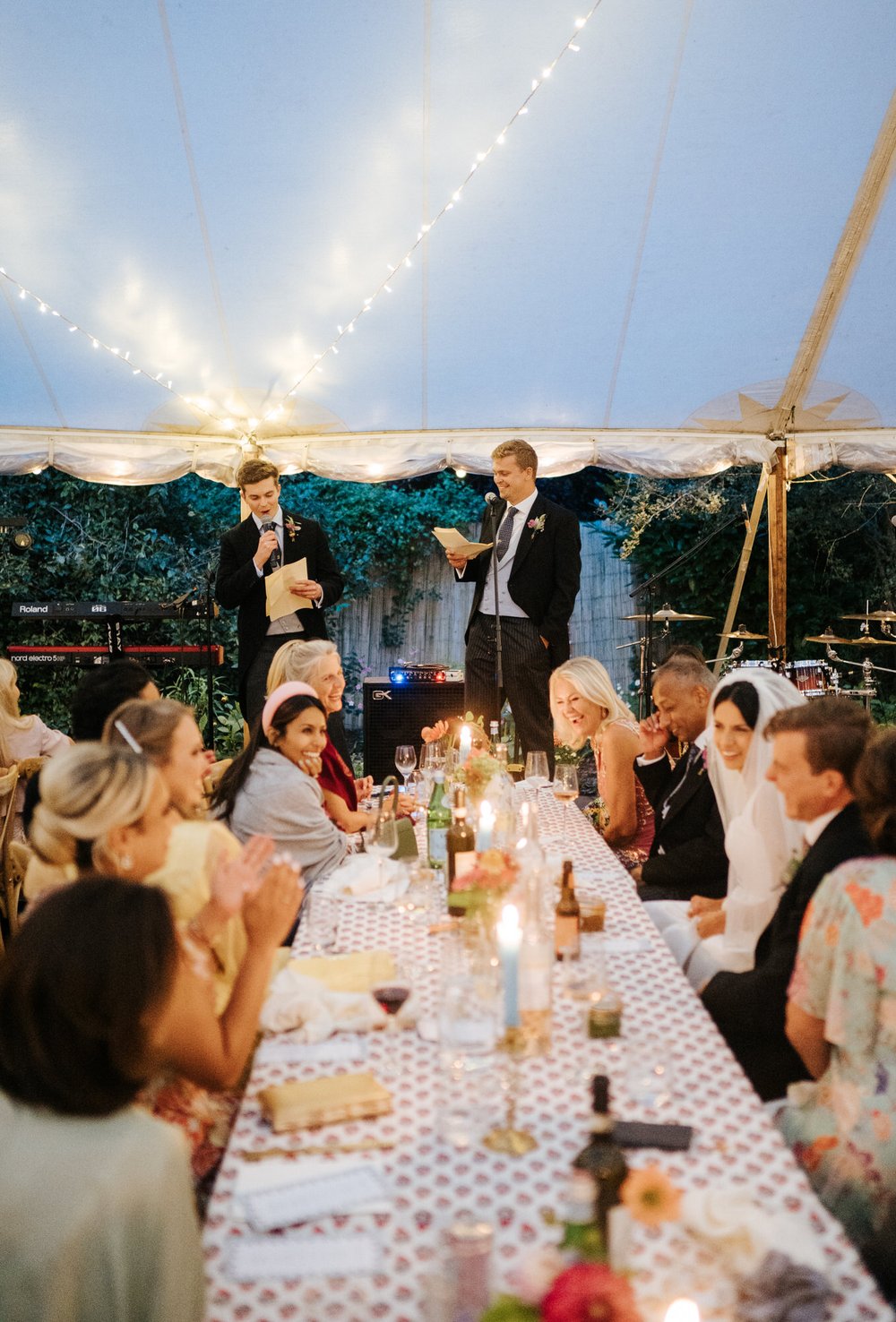 Groom's two brothers take stage and start delivering their speeches as guests laugh in this British garden wedding