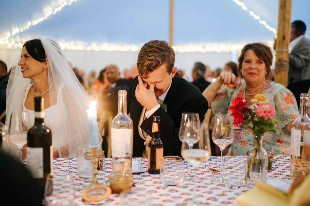 Groom covers his face in embarrassment as his brothers start delivering wedding speech inside marquee