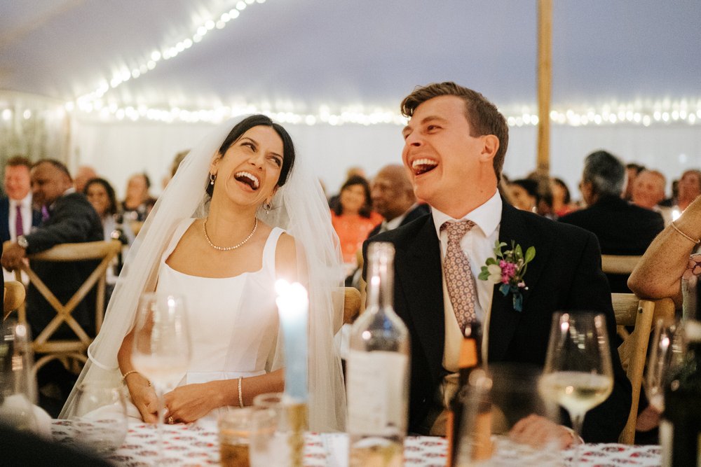 Bride and groom cannot contain their laughter as they look at each other during wedding speeches