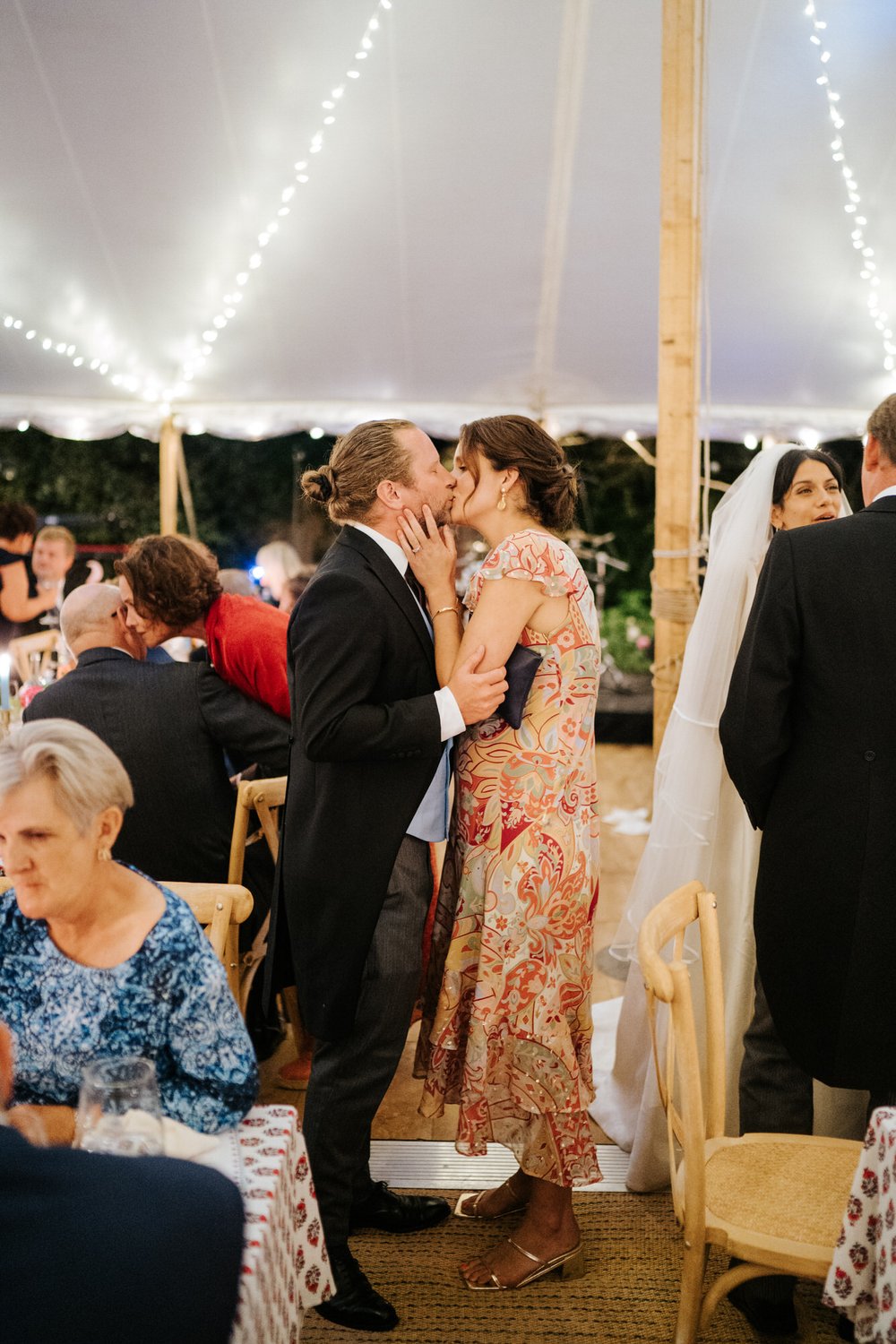 Two guests kiss and embrace in sneaky candid photograph taken during break after wedding speeches took place