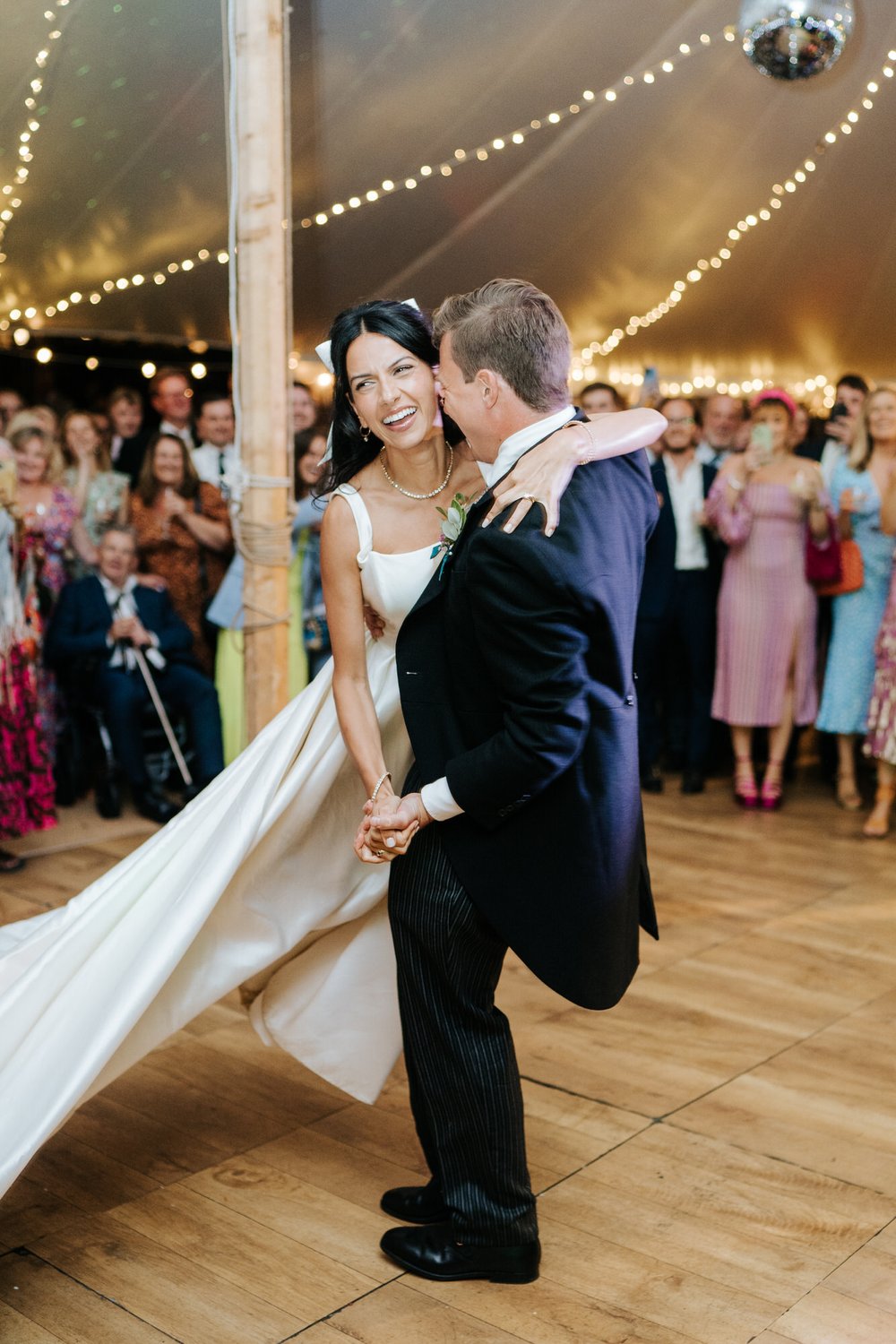 Groom lifts up the bride and swirls her along the dancefloor as she looks on excitedly