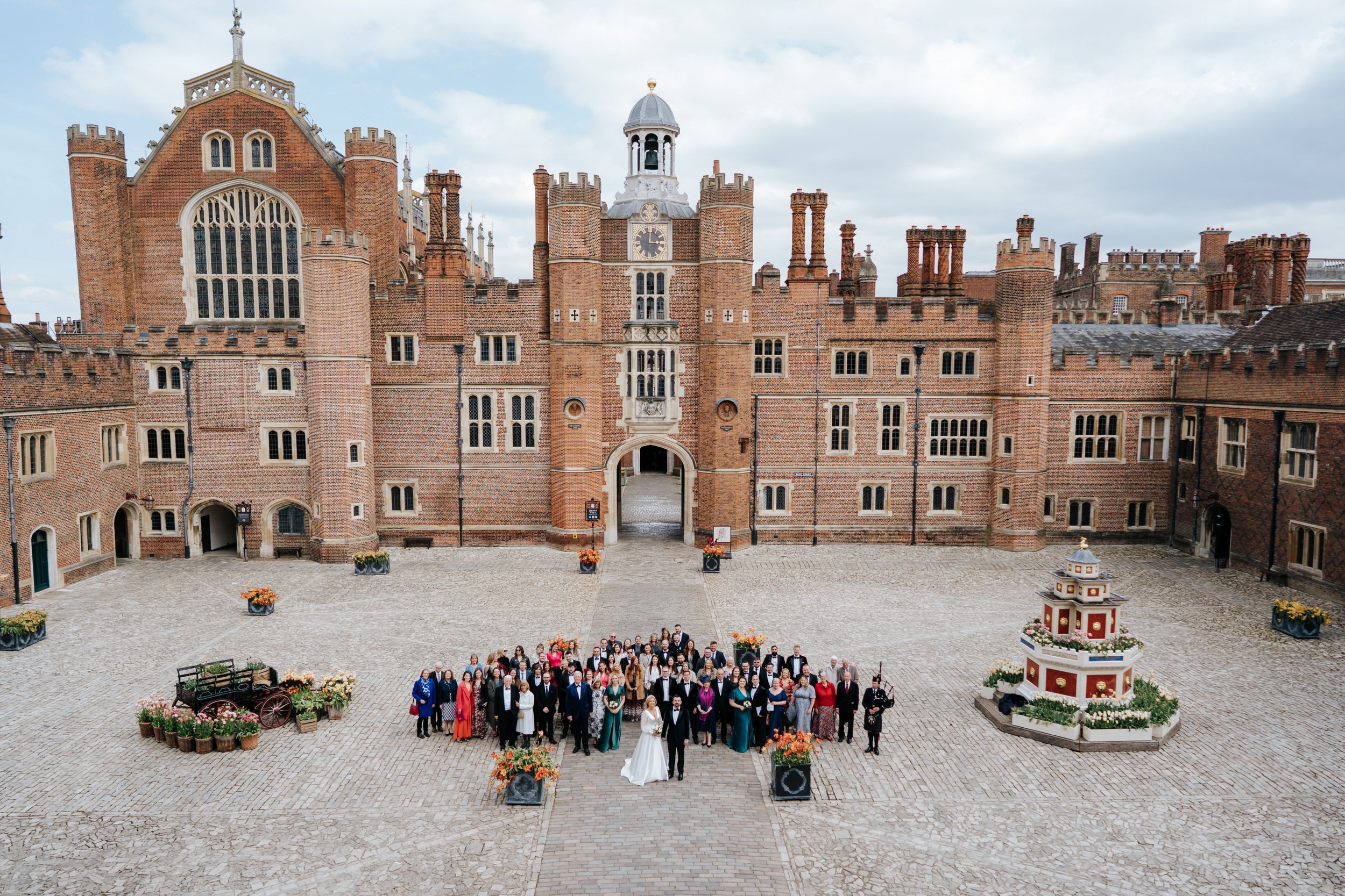 Wide shot of bride, groom and all the weddings guests in the courtyard at Hampton Court Palace