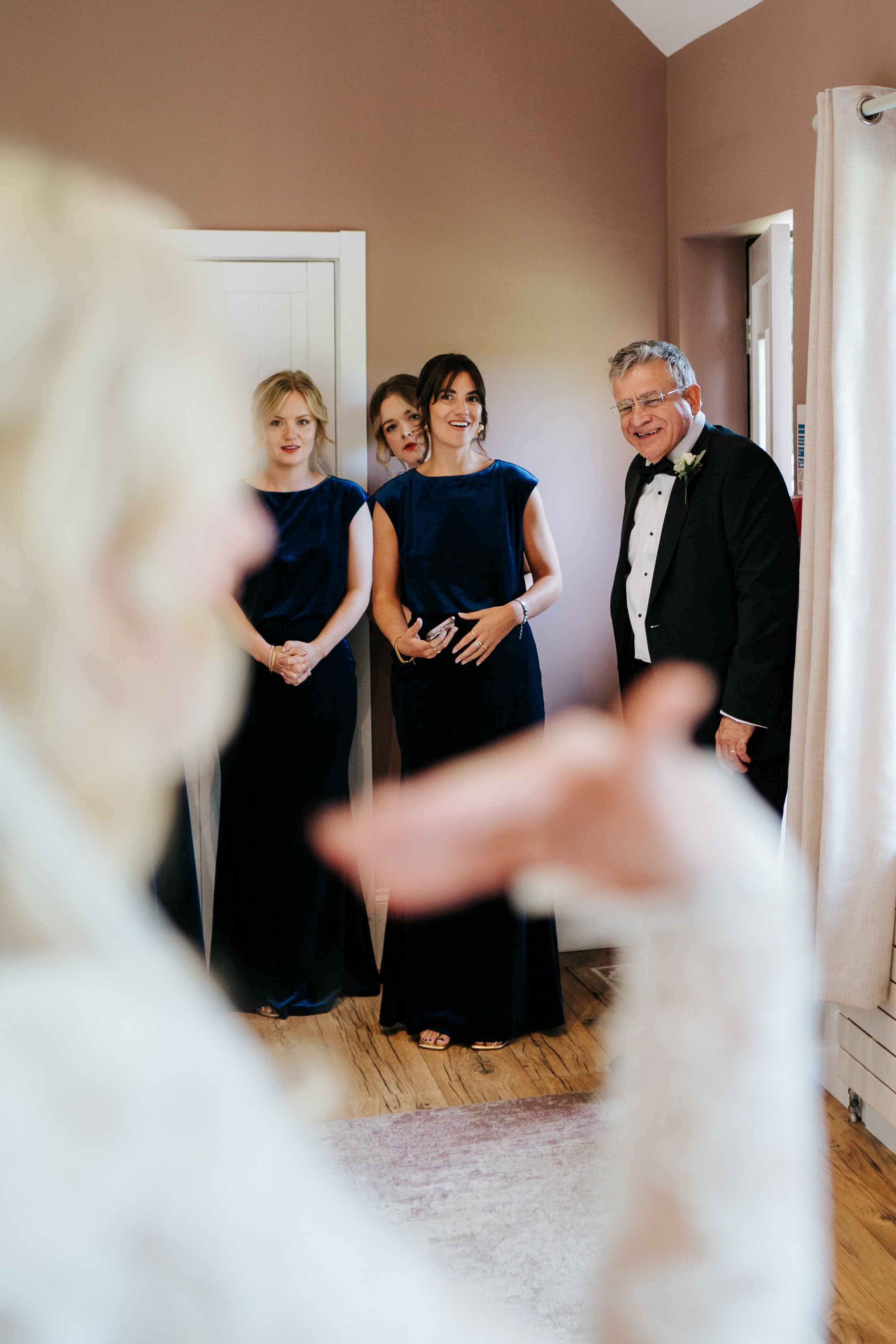 Father of the bride enters room to see his daughter in wedding dress for the first time as she raises hand to fan herself