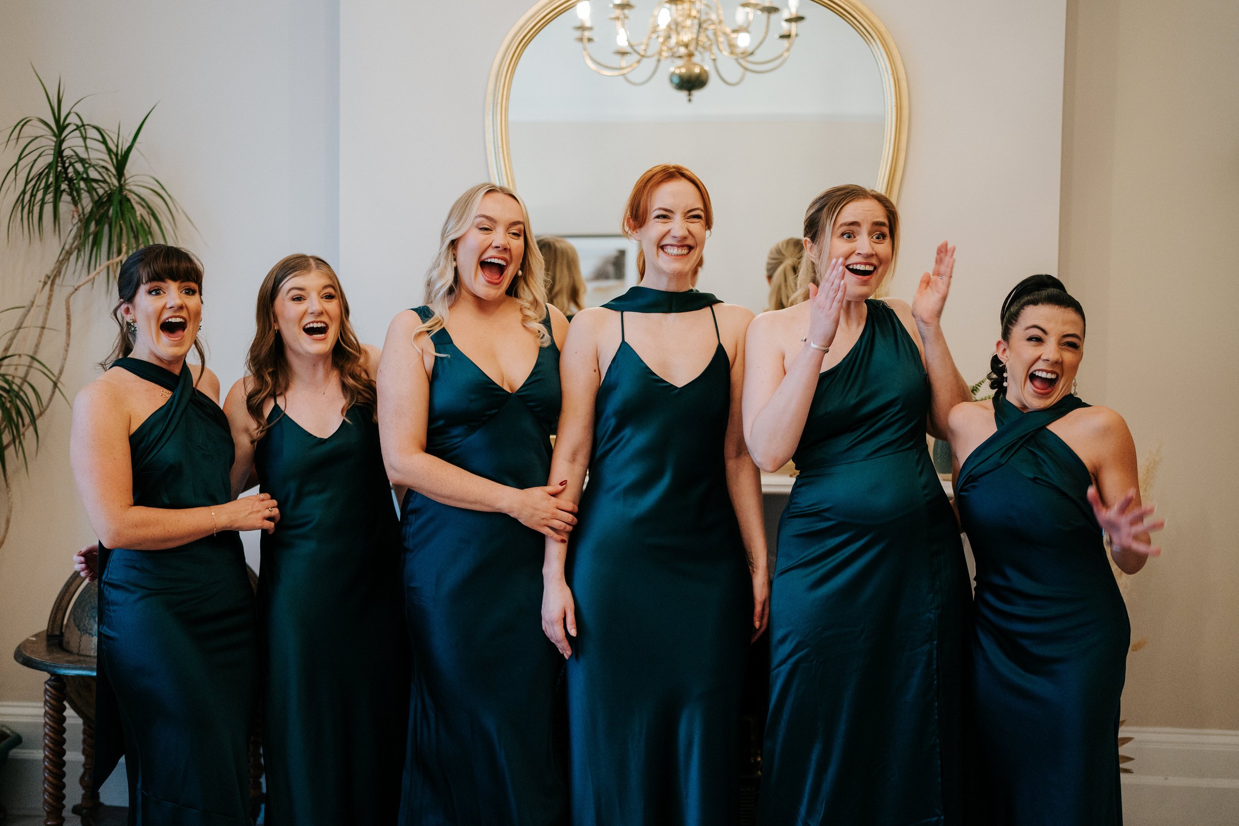 Six bridesmaids, lined up, react to seeing bride in her wedding dress for the first time