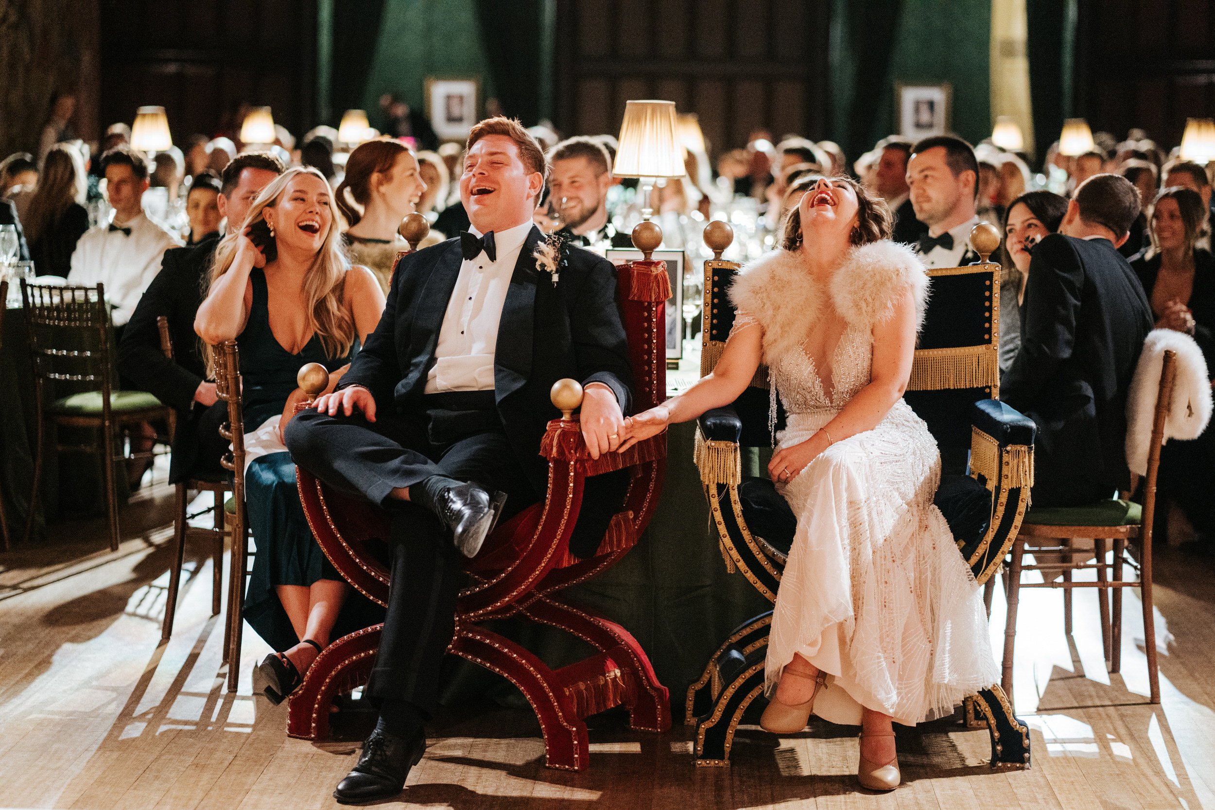 Bride and groom, sitting on throne seats, react to wedding speeches with excitement at Hampton Court Palace