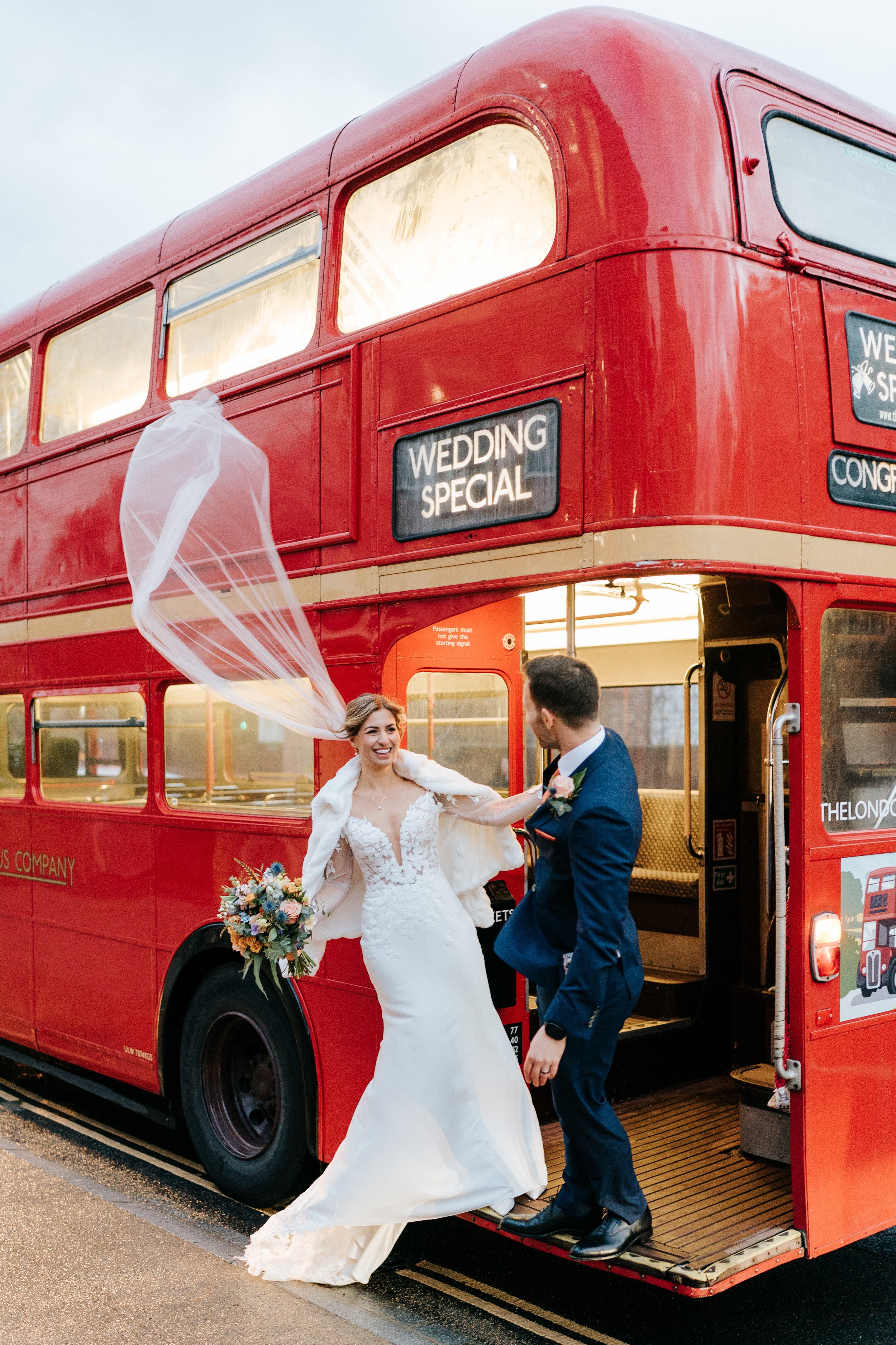 Bride and groom lean out of double-decker London bus as her veil floats into the London sky