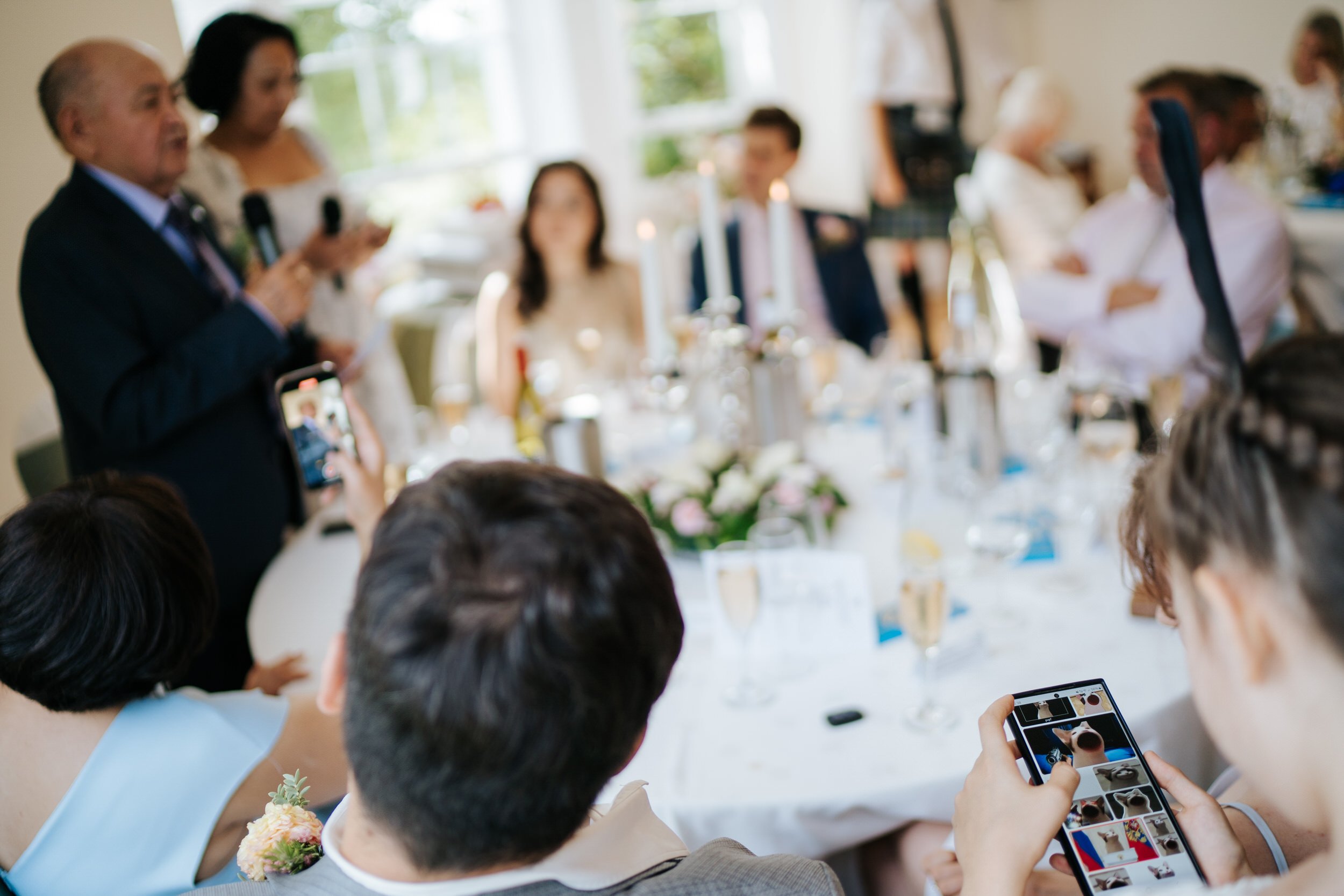 Speeches are delivered while young girl looks at funny memes on her phone at Pembroke Lodge wedding