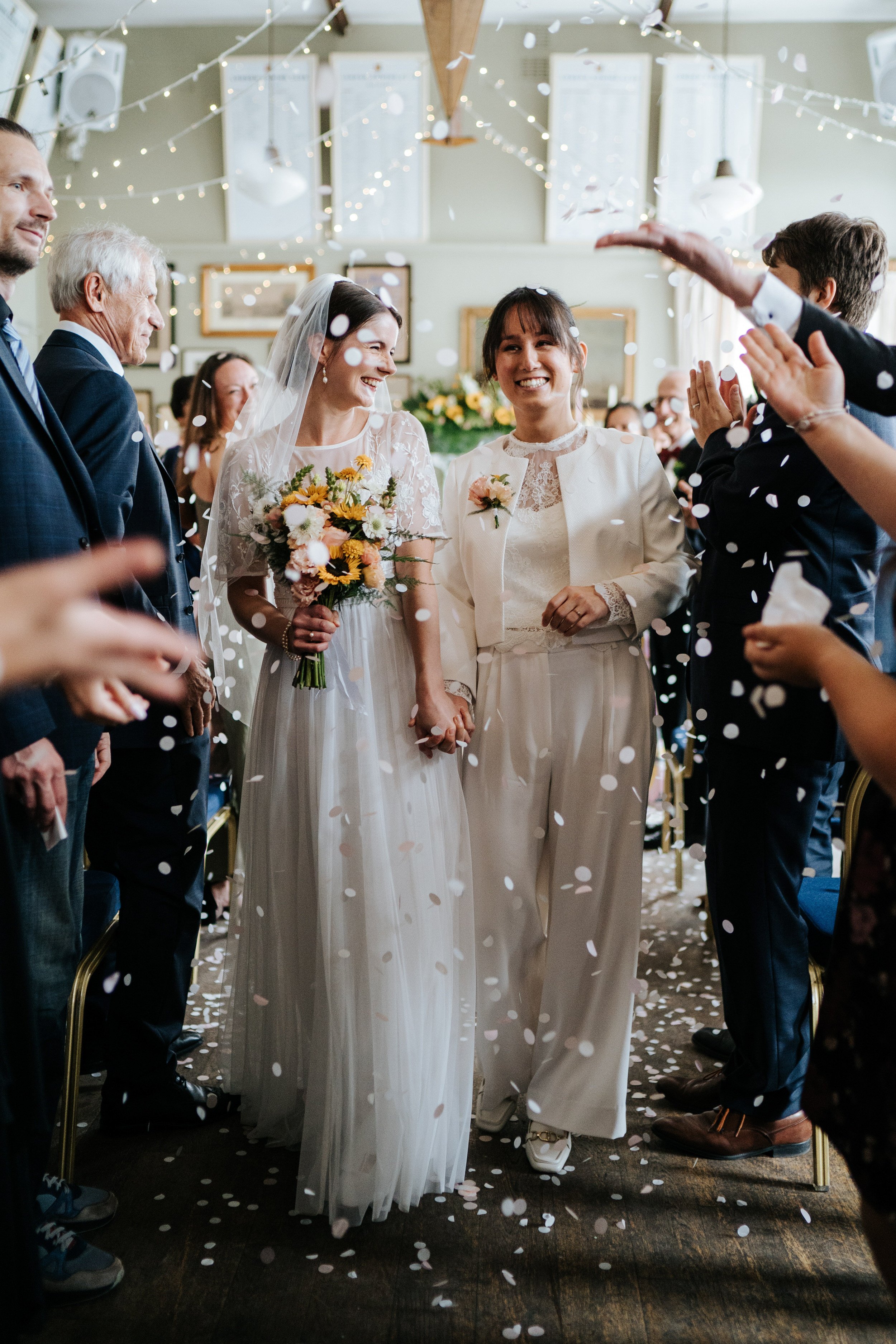 Two brides walk back down the aisle at Putney Rowing Club in beautiful confetti photograph