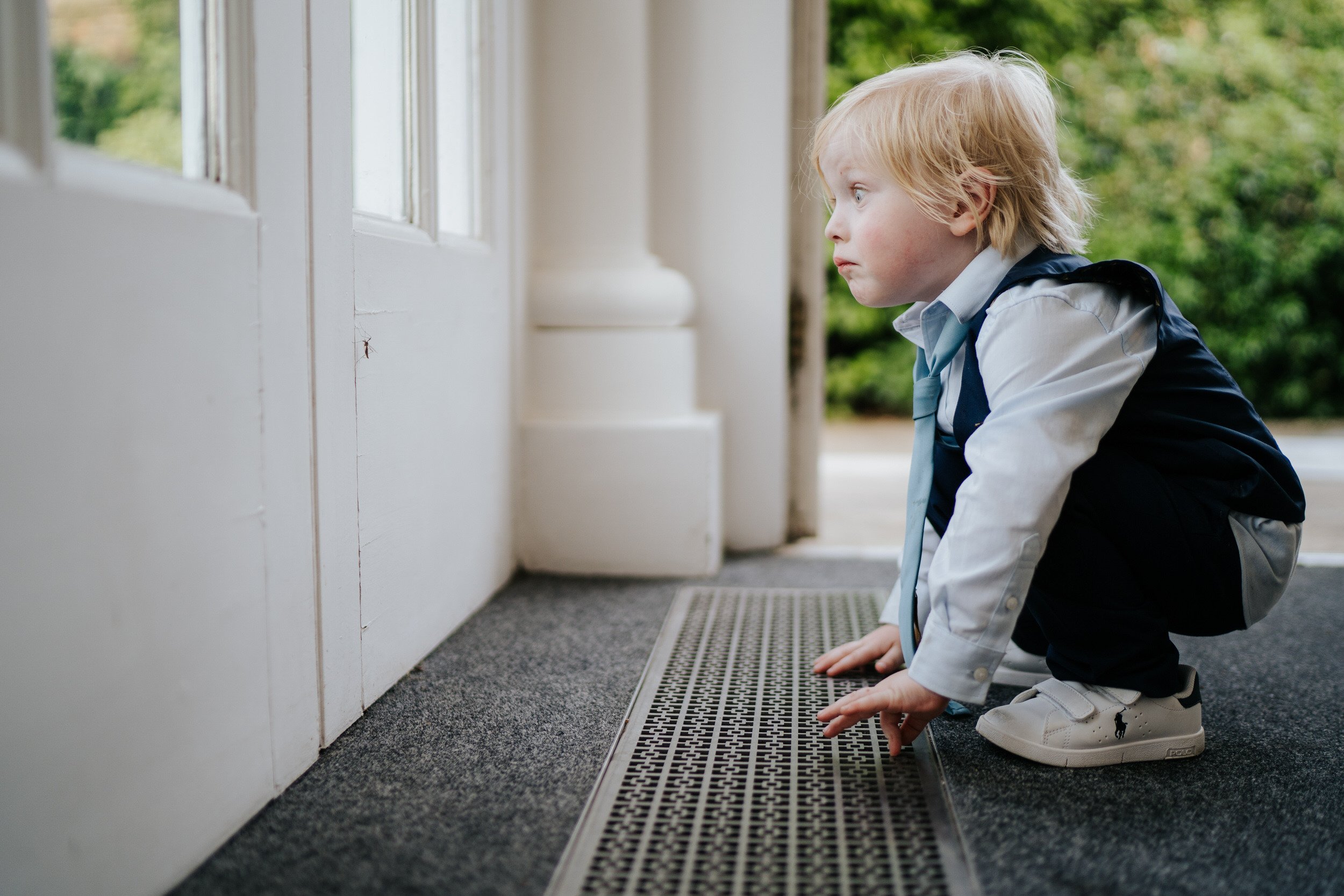 Little boy crouches in front of wall and looks in amazement at mosquito perched on wall in front of him