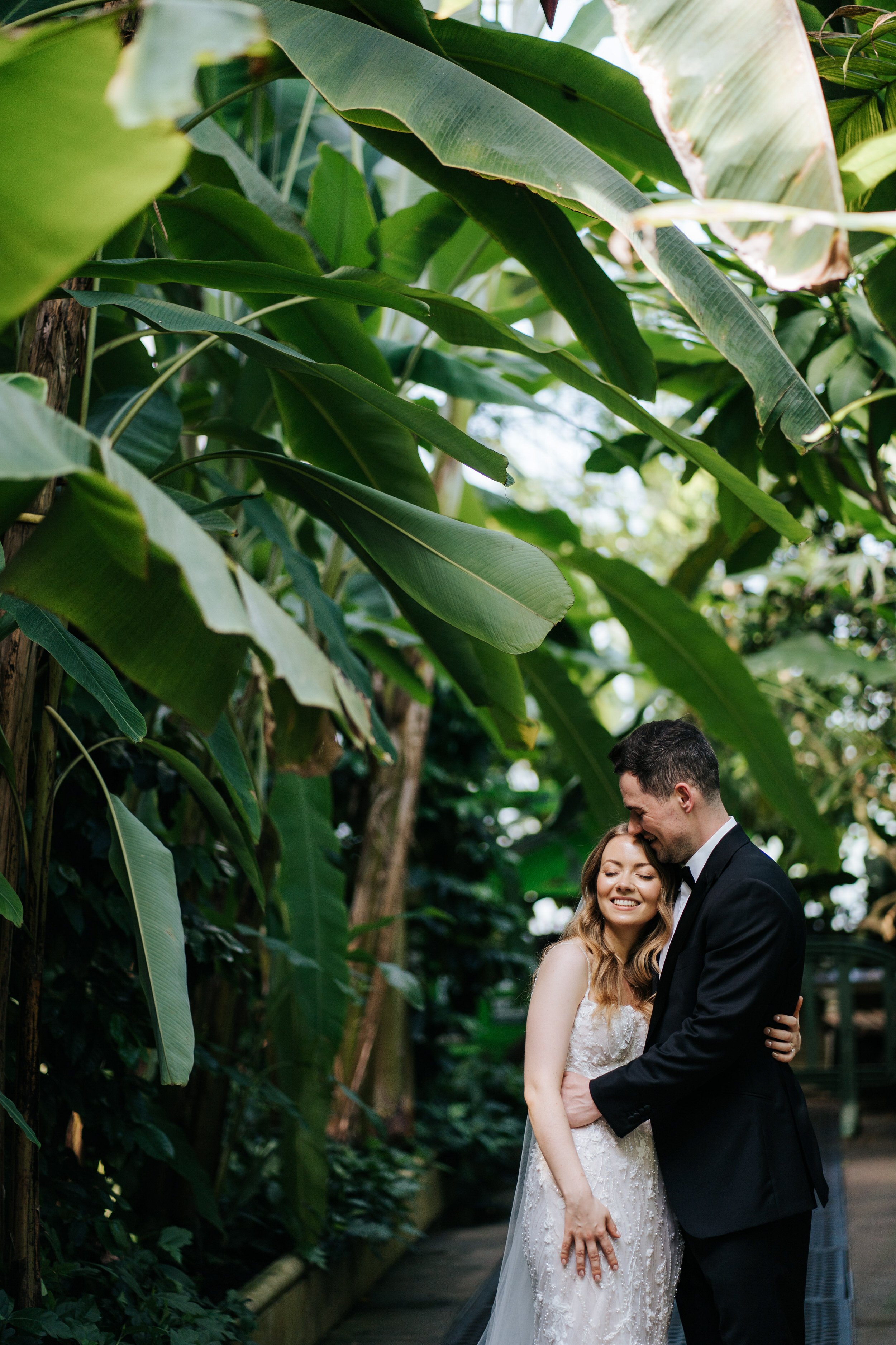 Bride and groom pose under palm trees in Temperate House at Kew Gardens