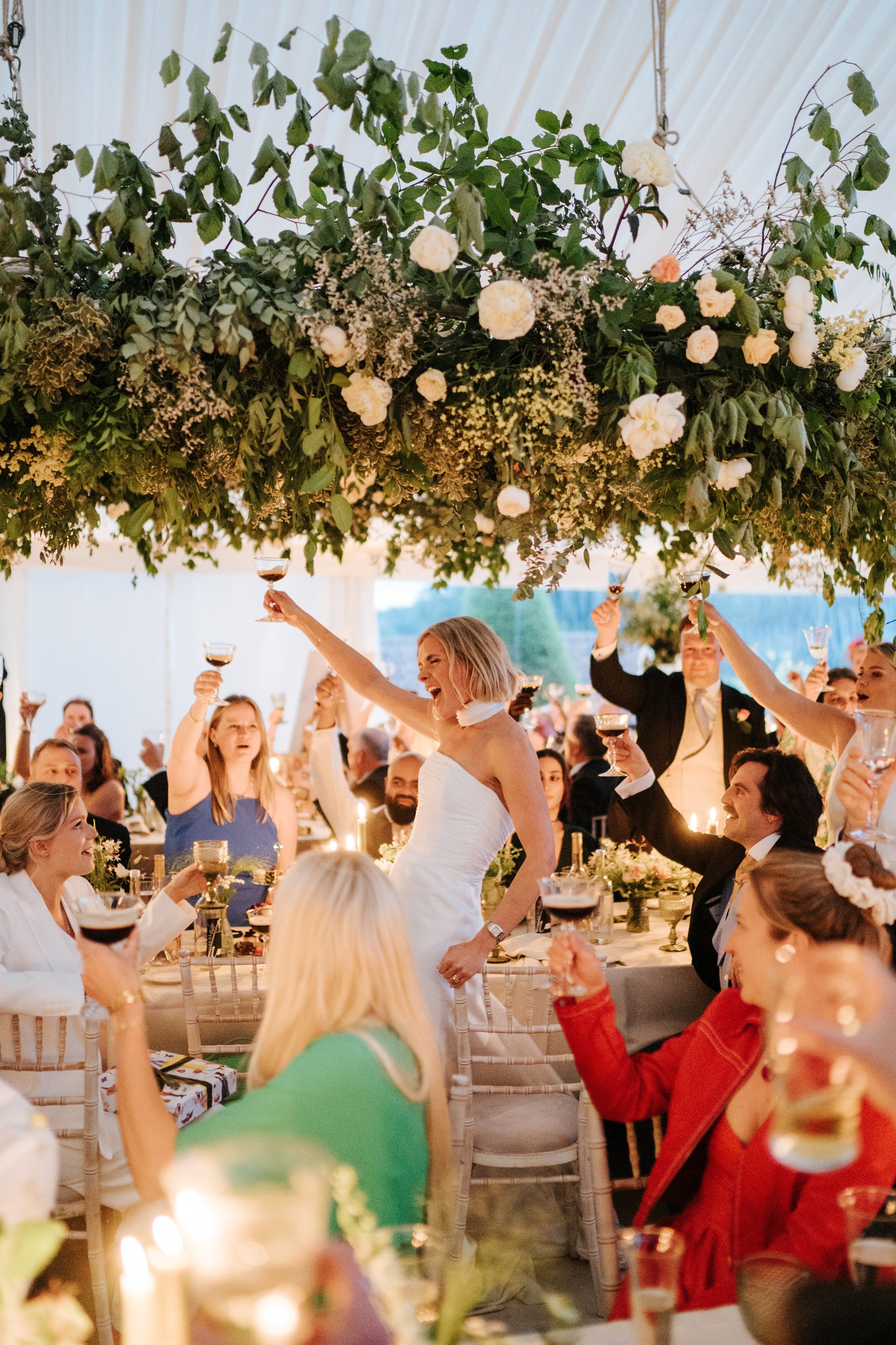 Epic photograph of bride standing up and toasting all of her guests after wedding speech in marquee garden wedding