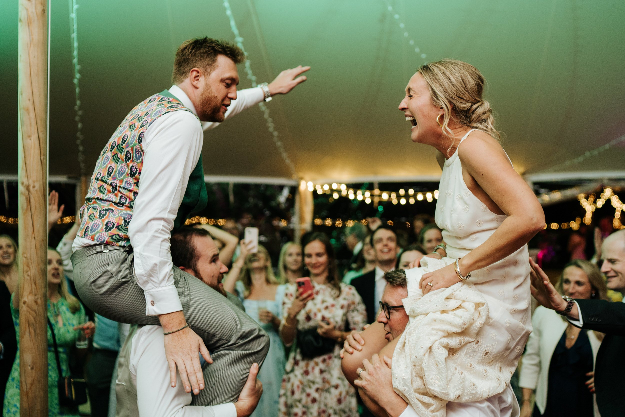 Bride and groom celebrate their wedding party as they sit on top of guests' shoulders