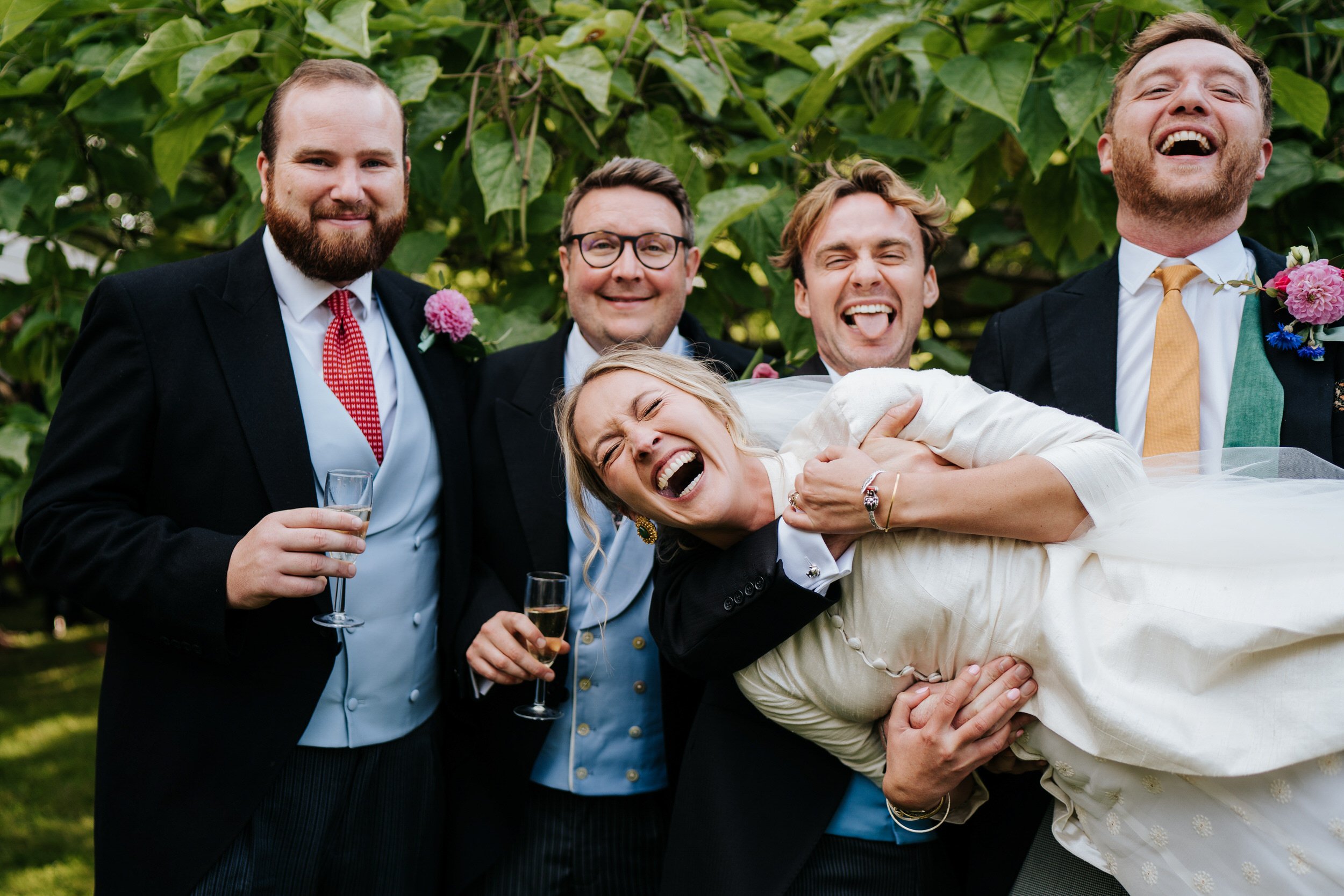 Bride smiles ear to ear as groom and ushers lift her up the ground and she lies across their arms