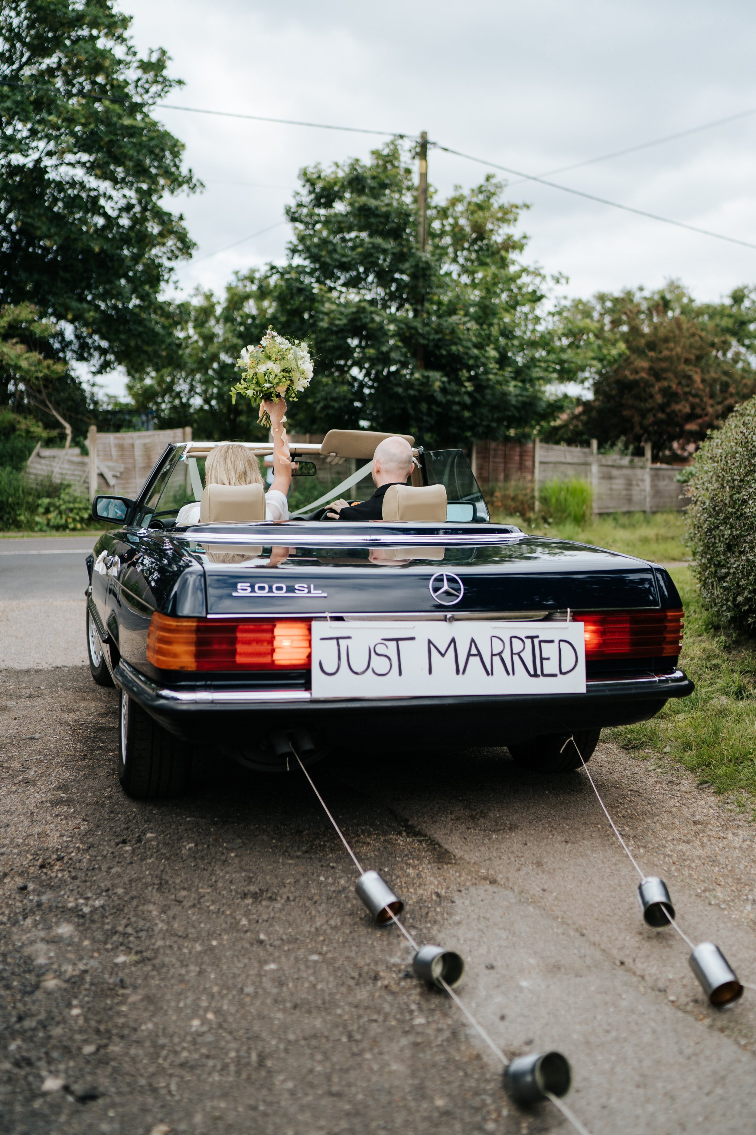 Bride and groom leave church in vintage convertible mercedes as bride lifts bouquet up